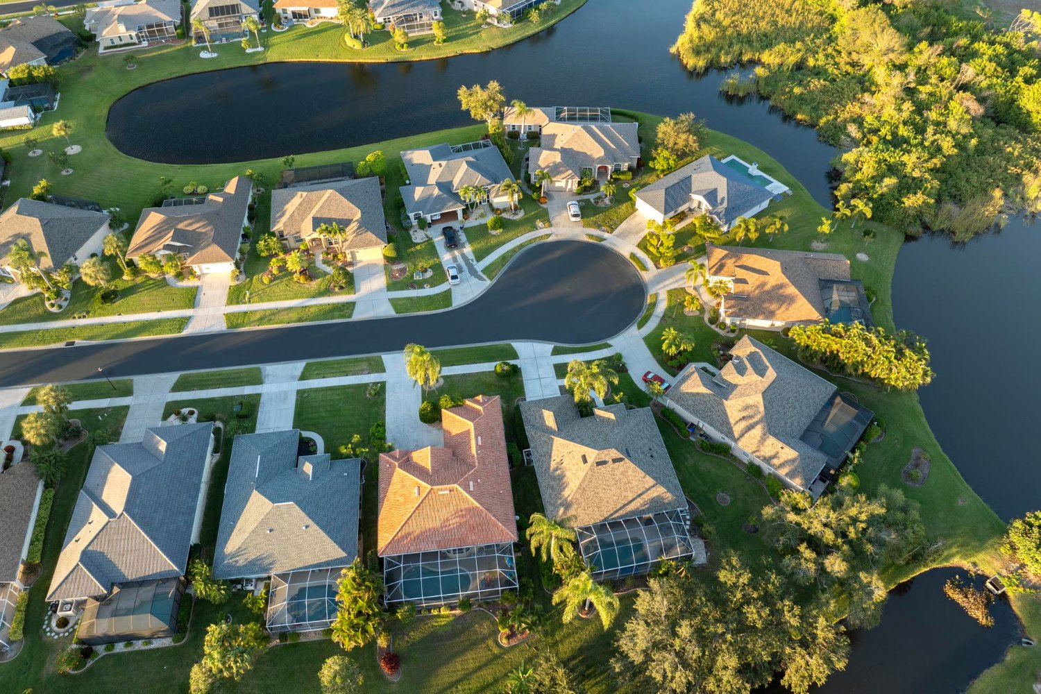 Aerial view of a residential neighborhood with houses, green lawns, trees, and a pond, featuring cul-de-sacs and street curves.
