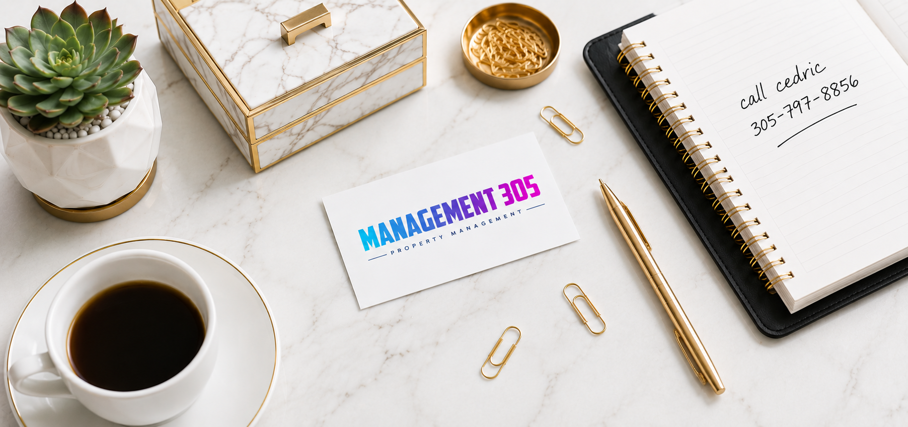 A workspace with a plant, a coffee cup, a gold pen, a notebook with a handwritten note, a business card reading "Management 305 Property Management," gold paper clips, a small gold dish with clips, a marble box with a gold handle, and a gold-trimmed container with paperclips, all arranged neatly on a white marble surface.