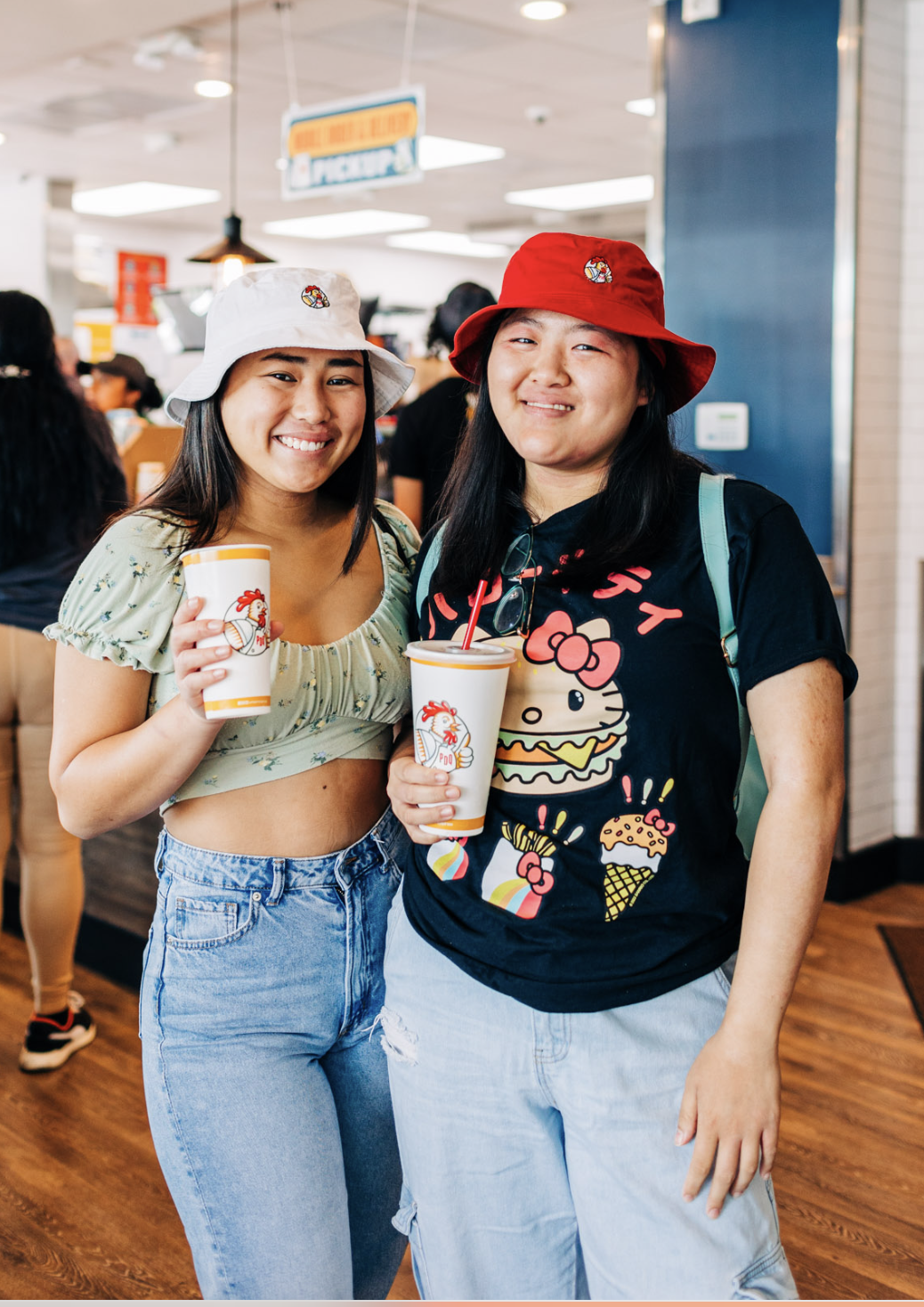 Two people wearing bucket hats and holding drinks in a fast-food restaurant.