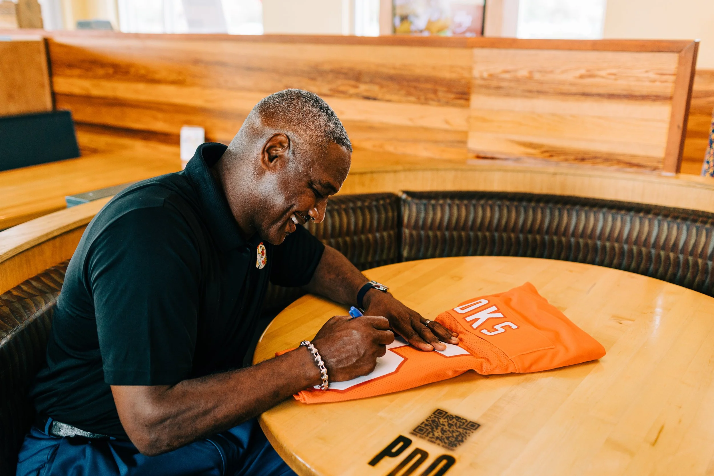 Person signing an orange sports jersey on a wooden table in a restaurant.
