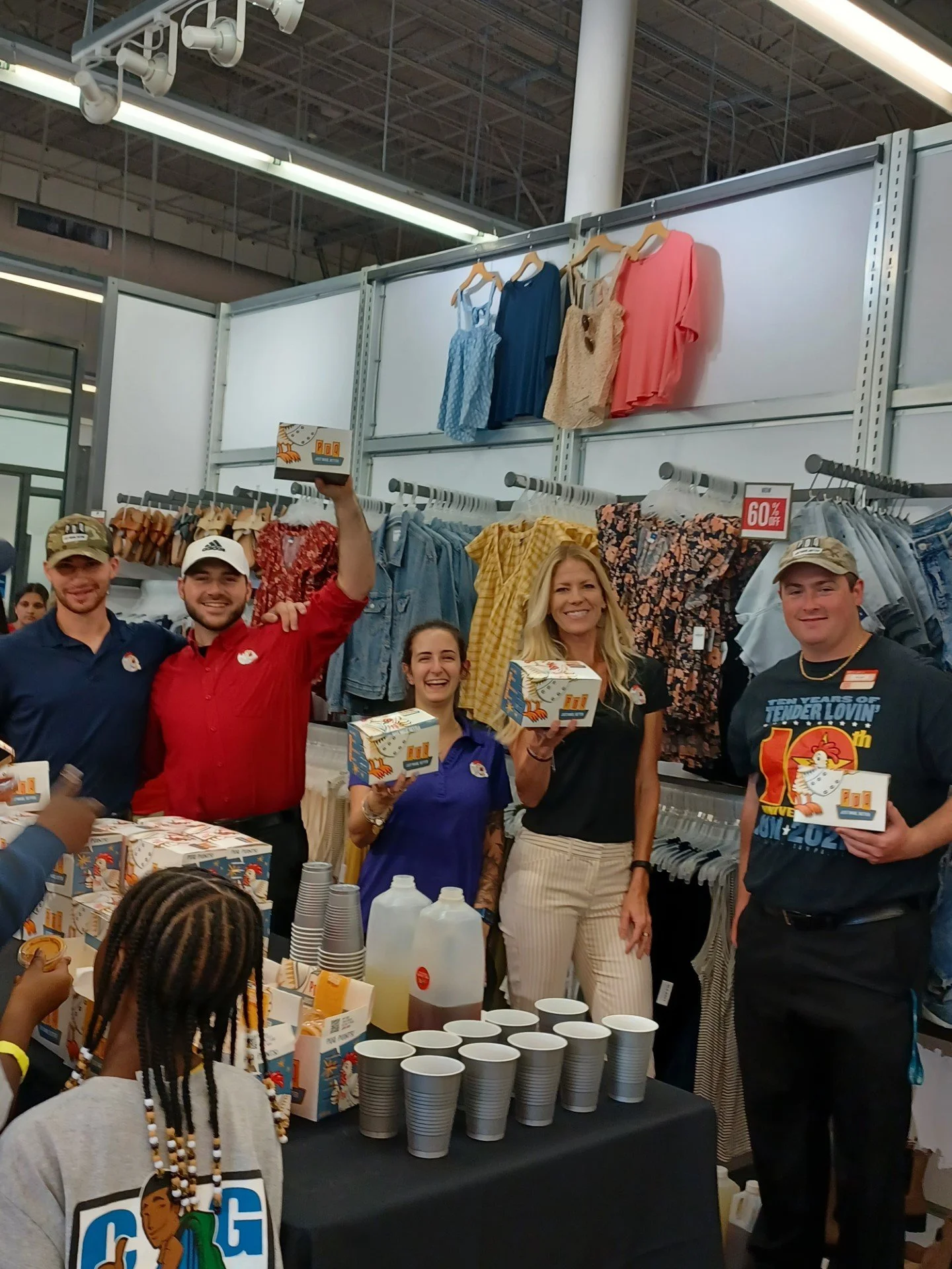 Group of people holding merchandise boxes in a retail clothing store with a display of drinks on a table.