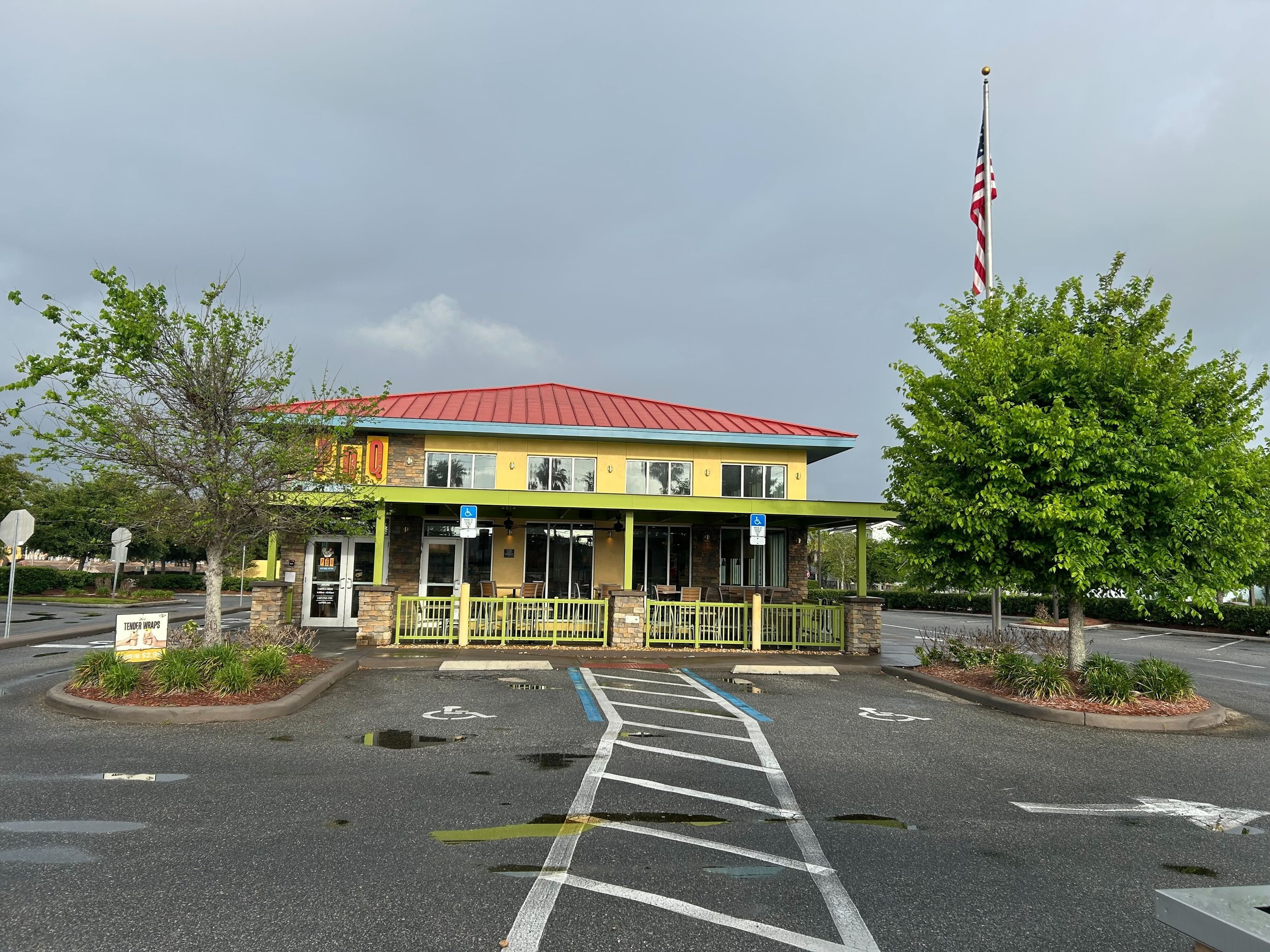 Empty parking lot in front of a restaurant with a red roof, yellow walls, and large windows; there are two handicap parking spaces and a sign for tender wraps.