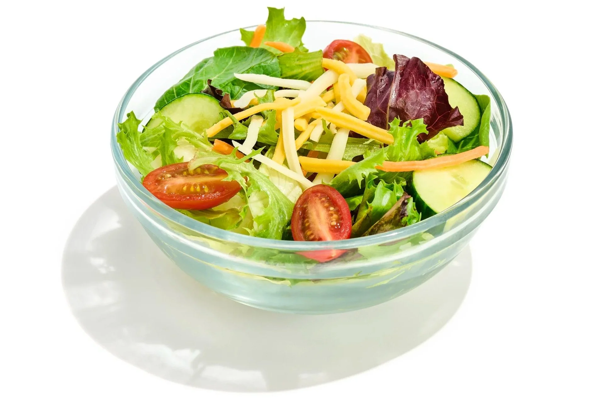 Fresh mixed salad in a glass bowl with cherry tomatoes, cucumber slices, lettuce, and shredded cheese.