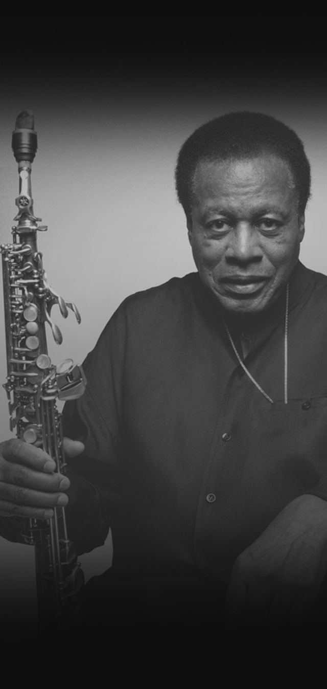 Black and white photo of a man holding a clarinet, wearing a dark shirt, with a neutral expression on his face.
