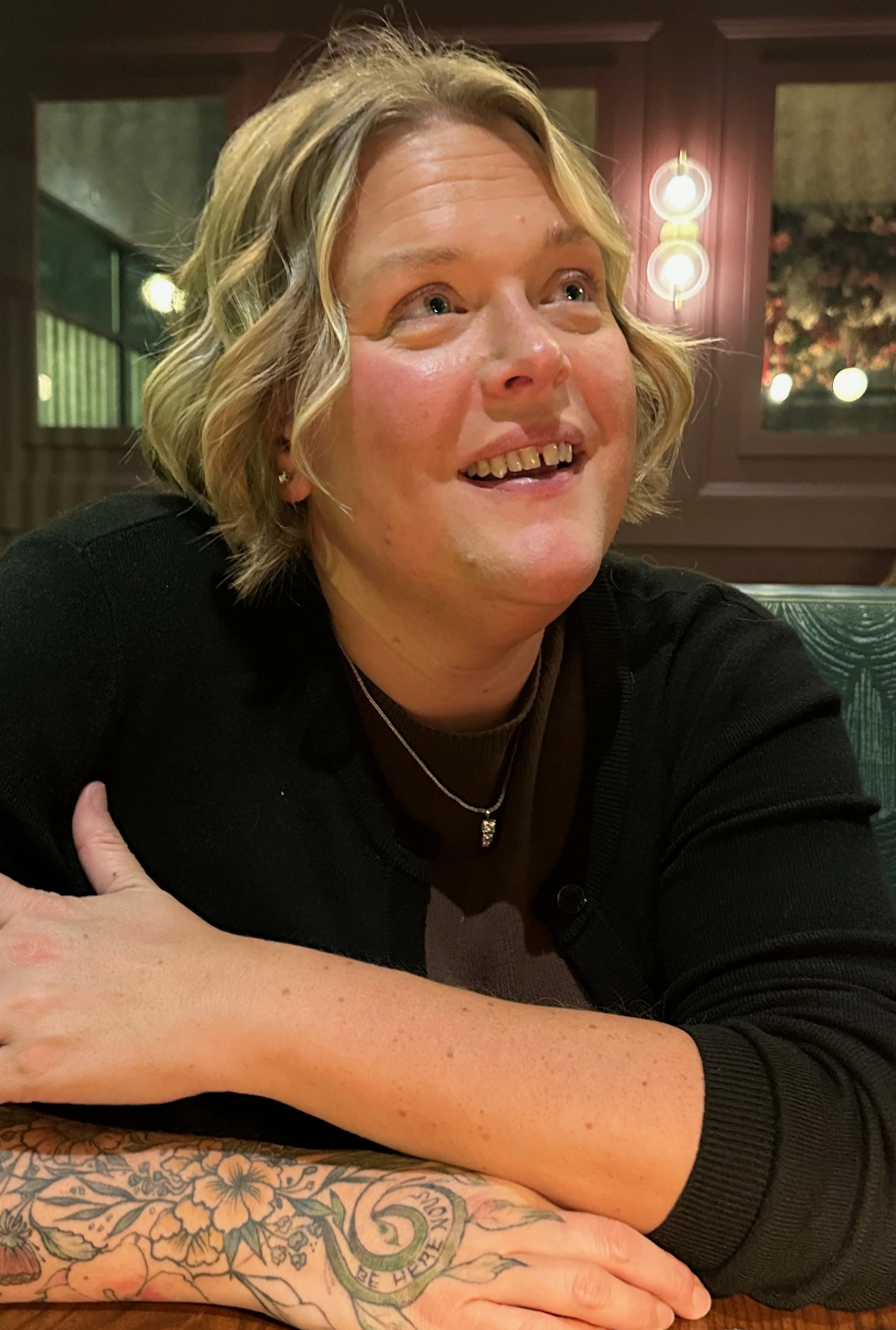 A smiling woman with blonde hair sitting at a table in a restaurant.