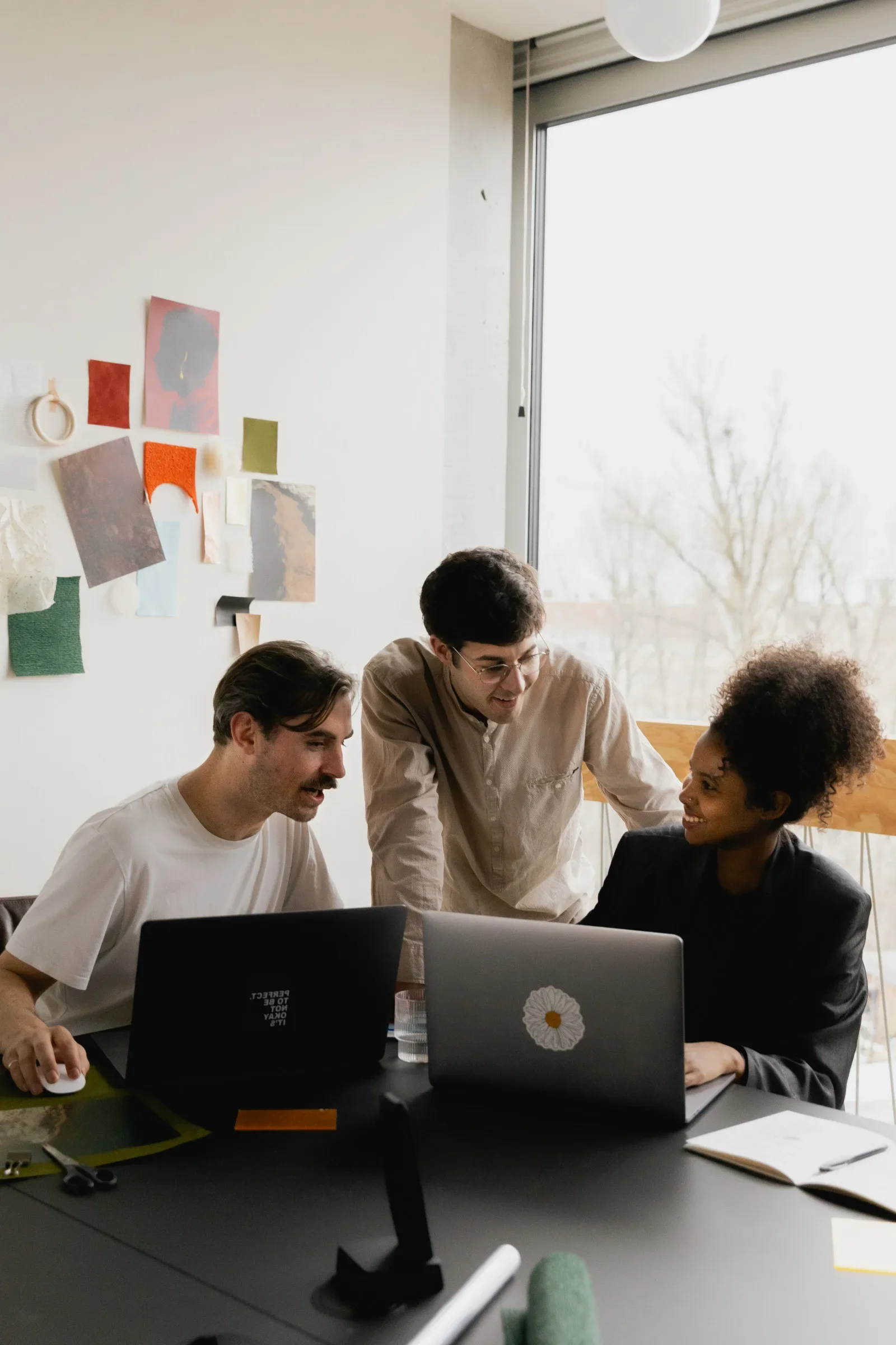 IT consulting team of three collaborating around two laptops in a bright office