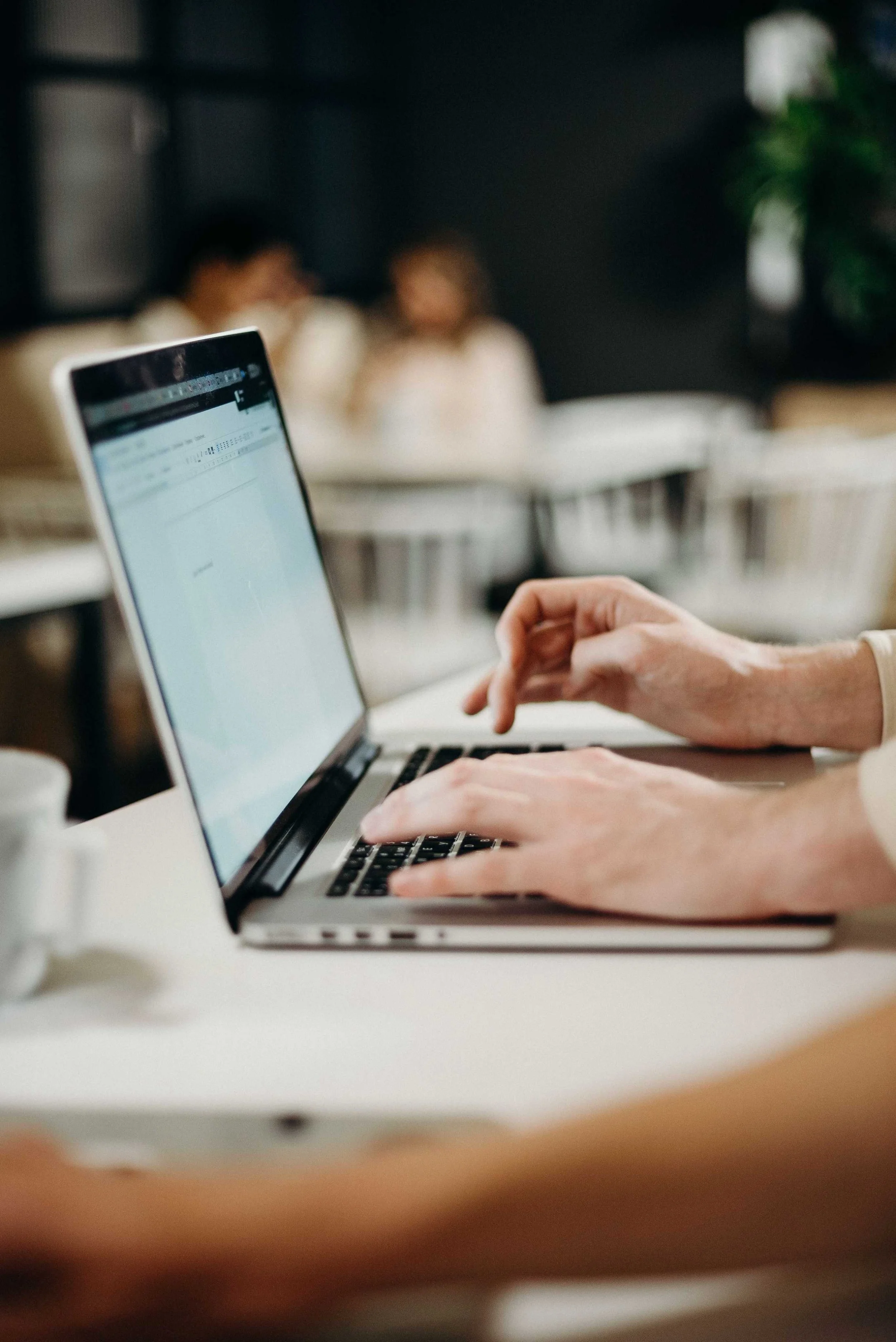 Hands typing on a laptop in a coffee shop