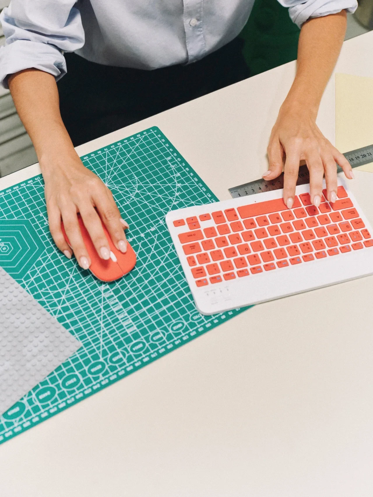 Close-up of hands typing on an orange keyboard next to a green cutting mat