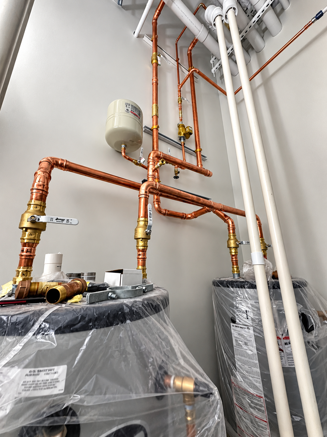 Interior of a mechanical room with copper pipes, white PVC pipes, and water heater units visible.
