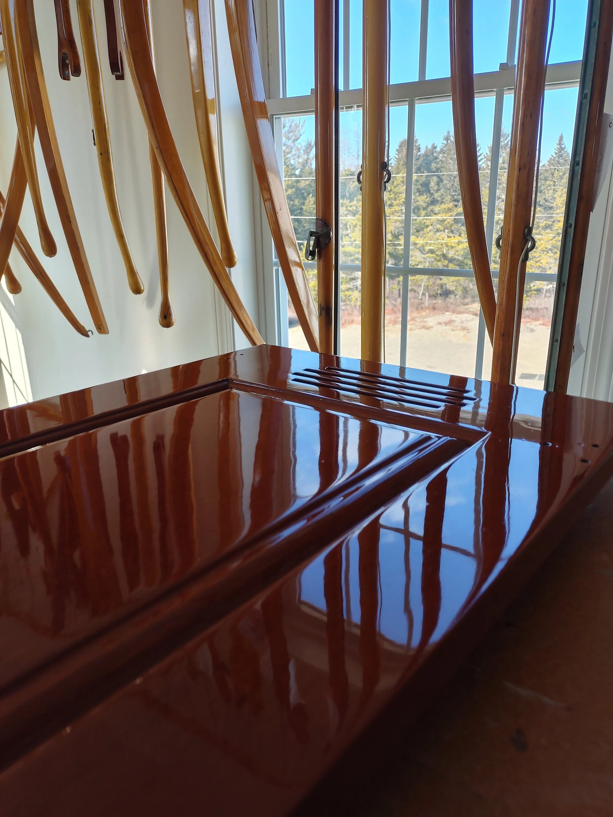 boat tiller arms and cabinet doors stacked against a wall near a window with a view of trees and clear blue sky.