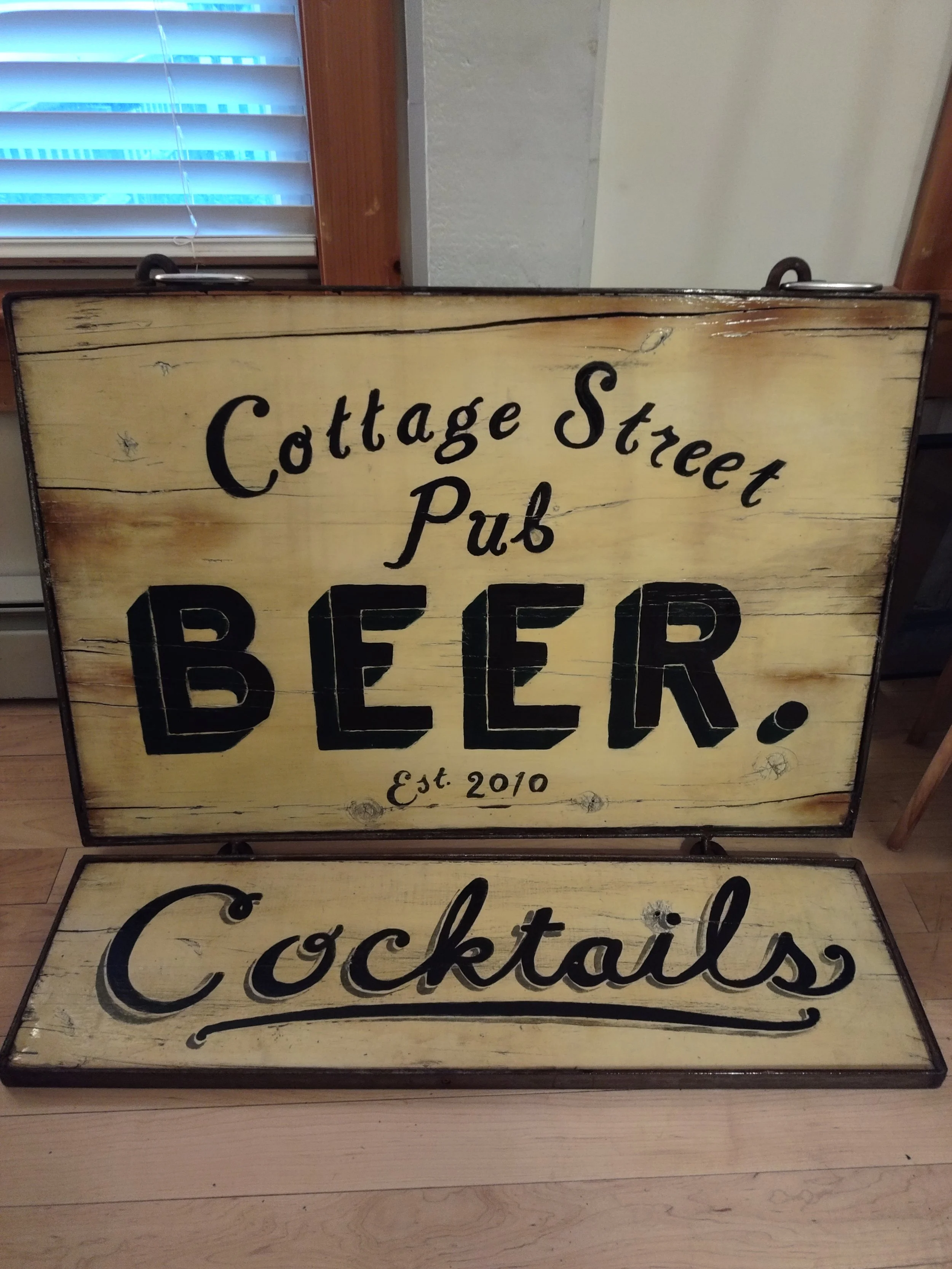 Decorative wooden sign with black handwritten-style text advertising a pub showcasing hand lettered and hand painted sign details
