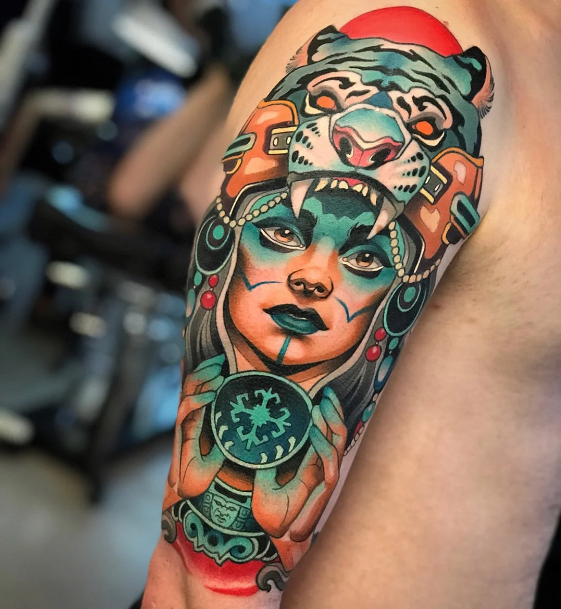 Colorful tattoo of a woman with dark makeup and face paint holding a circular symbol, wearing a headdress with a bear face and sun in the background. By Johnny Domus, Neo Traditional and Neo Japanese Tattoo.