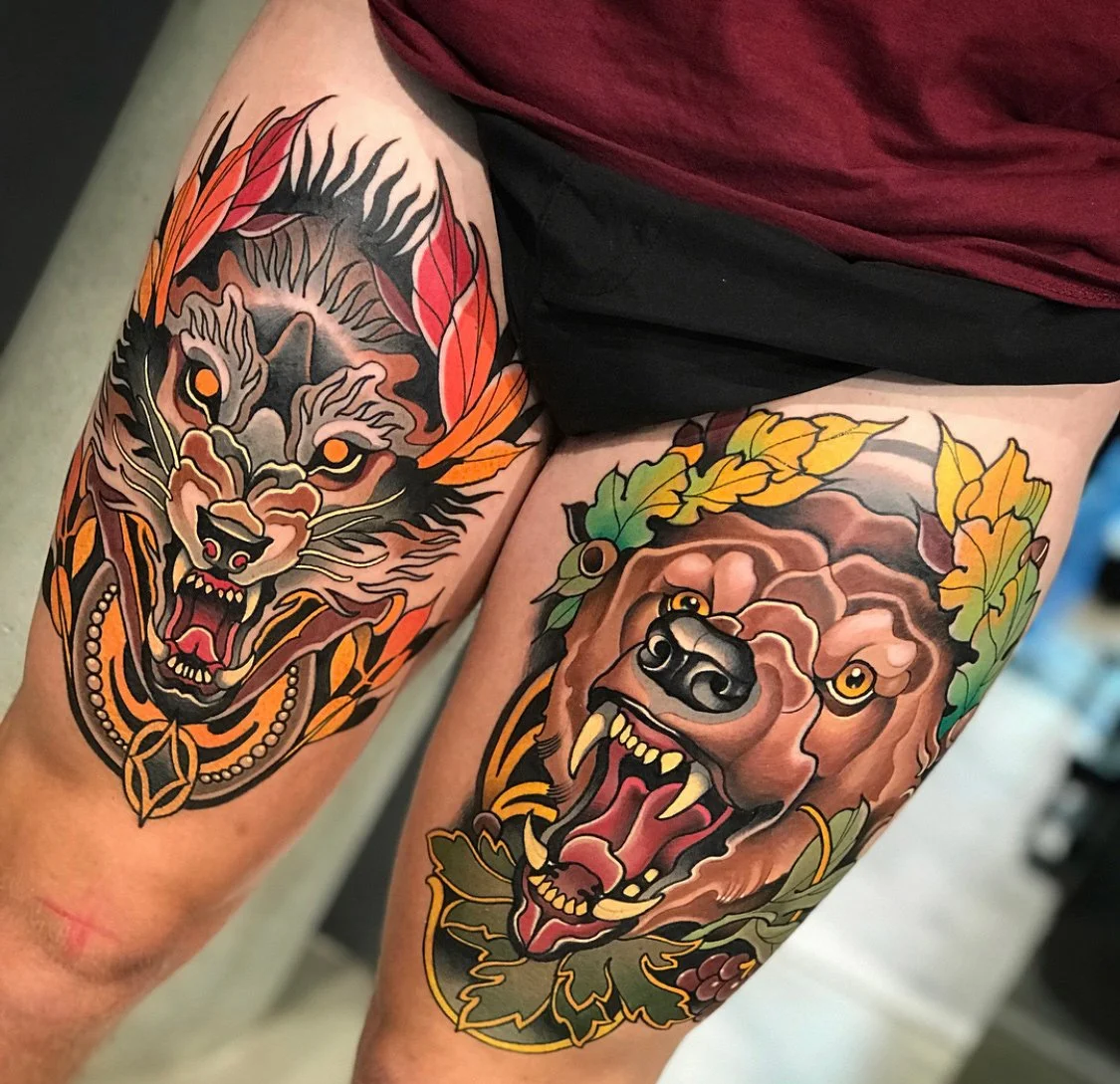 Tattoo of a fierce wolf on the left thigh and a roaring bear on the right thigh, both surrounded by colorful leaves. By Johnny Domus, Neo Traditional and Neo Japanese Tattoo.