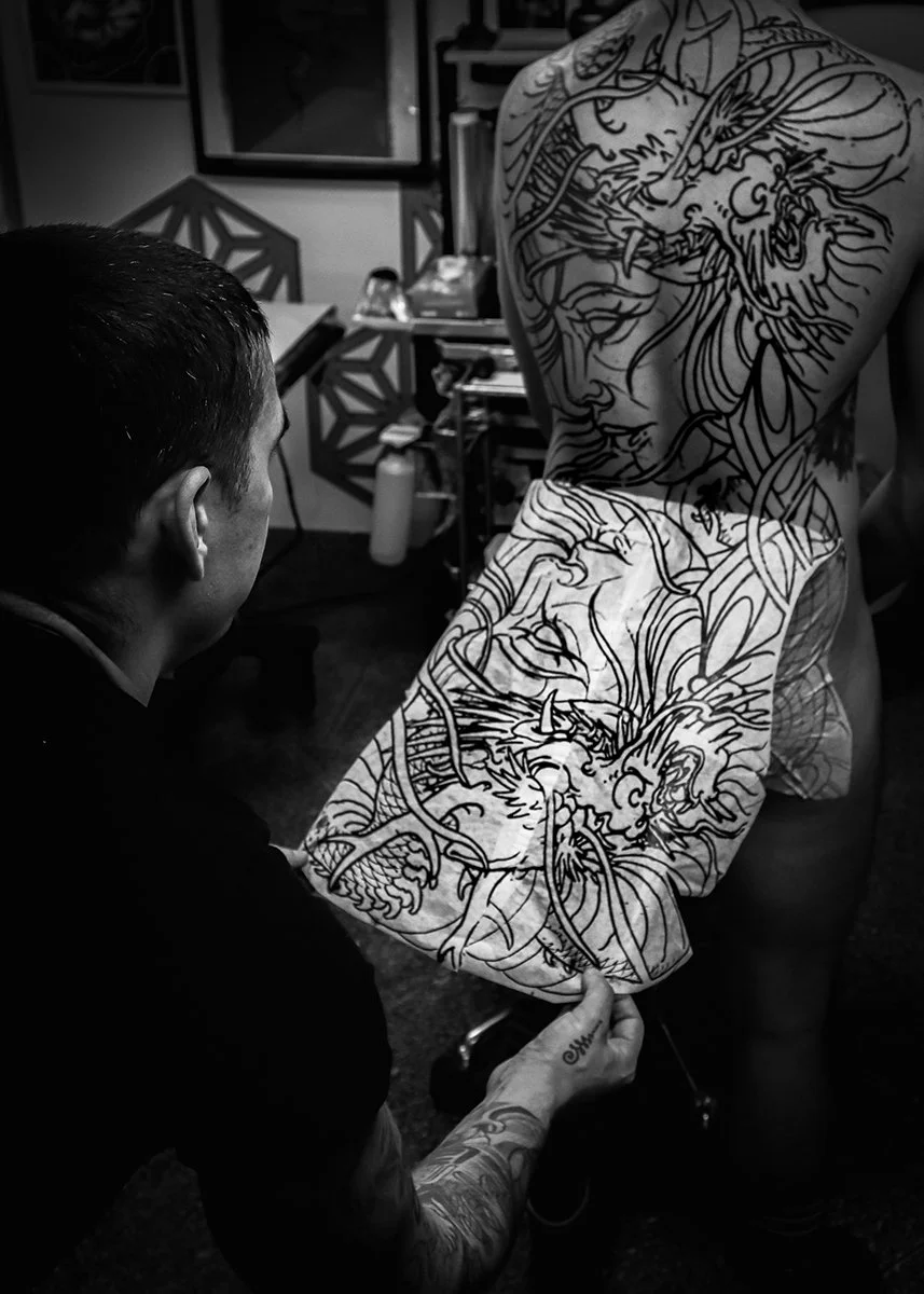 Tattoo artist creating a large dragon and female face tattoo on a person's back in a tattoo studio. By Johnny Domus, Neo Traditional and Neo Japanese Tattoo.