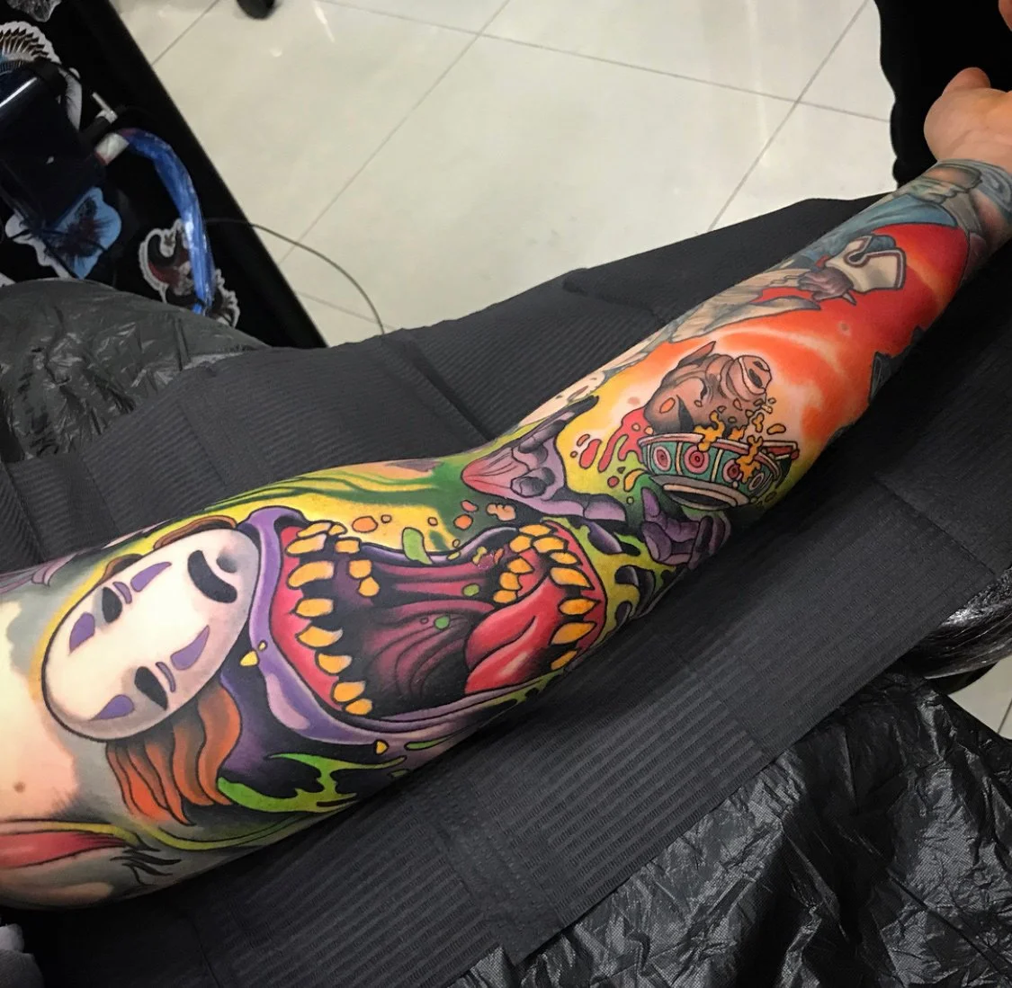 Colorful tattoo sleeve featuring a skull, a grinning face, a bowl of ramen noodles, and various abstract designs on a person's arm. By Johnny Domus, Neo Traditional and Neo Japanese Tattoo.