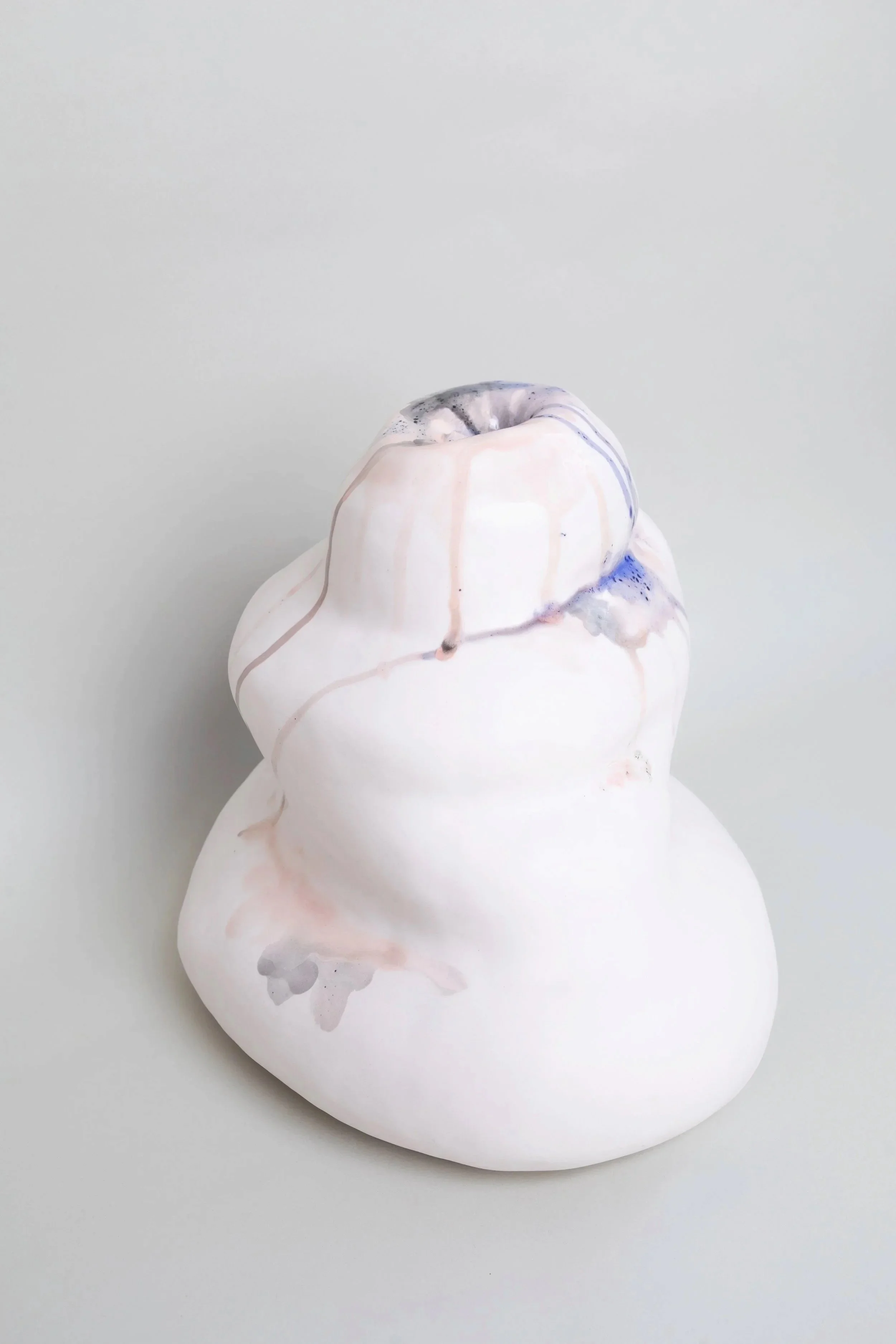 White soft curved ceramic sculpture with a hole at the top.  Pink black and purple glazes are dripped inside the hole and along the outside of the form.