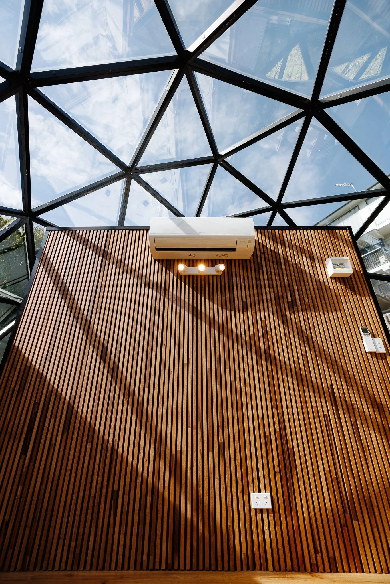 Luxury accommodation and Airbnb, Interior view of a room with an architectural glass ceiling, wooden slat wall, white air conditioning unit, lighting and electrical outlets.