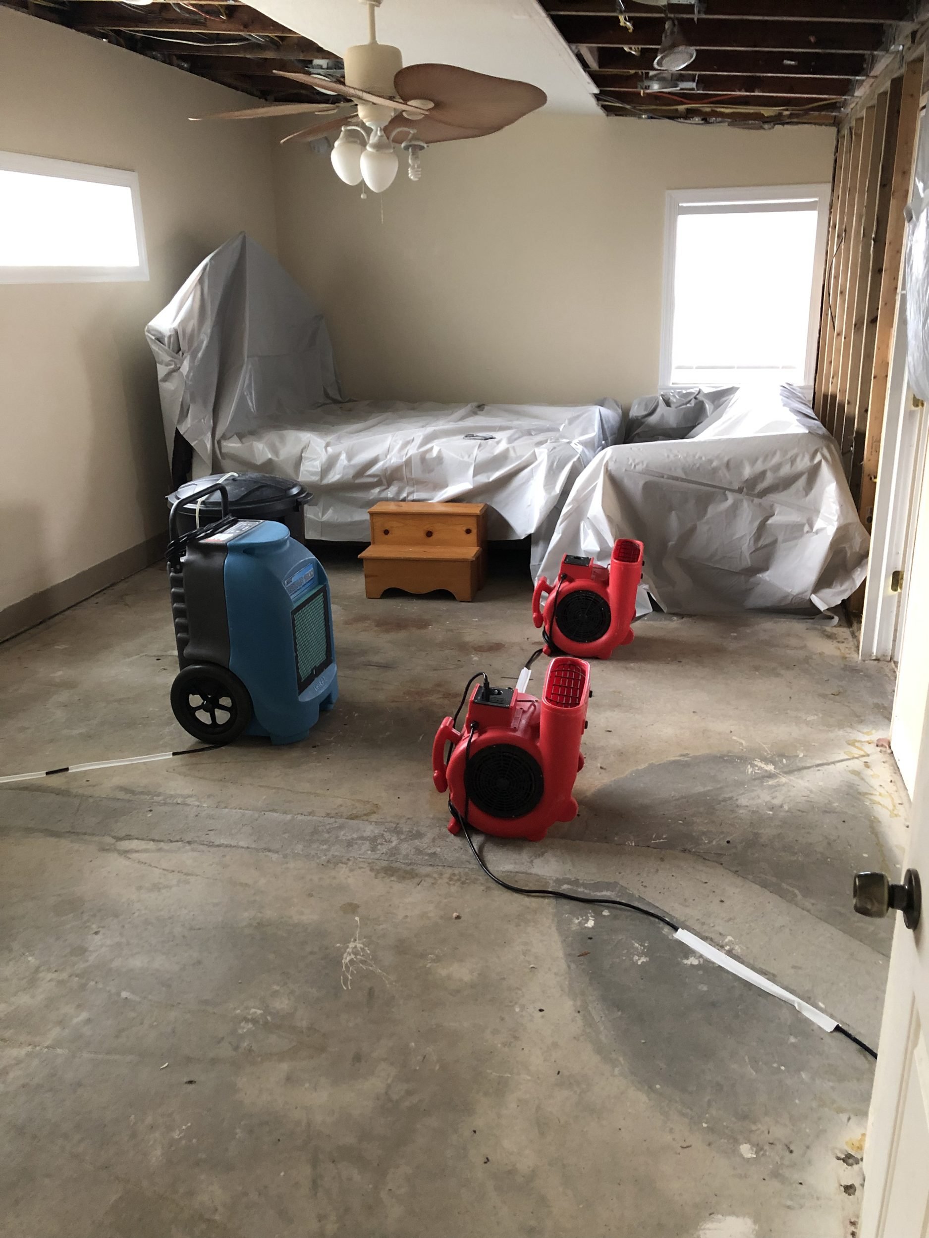 Air movers and dehumidifier drying a water-damaged bedroom with furniture protected under plastic