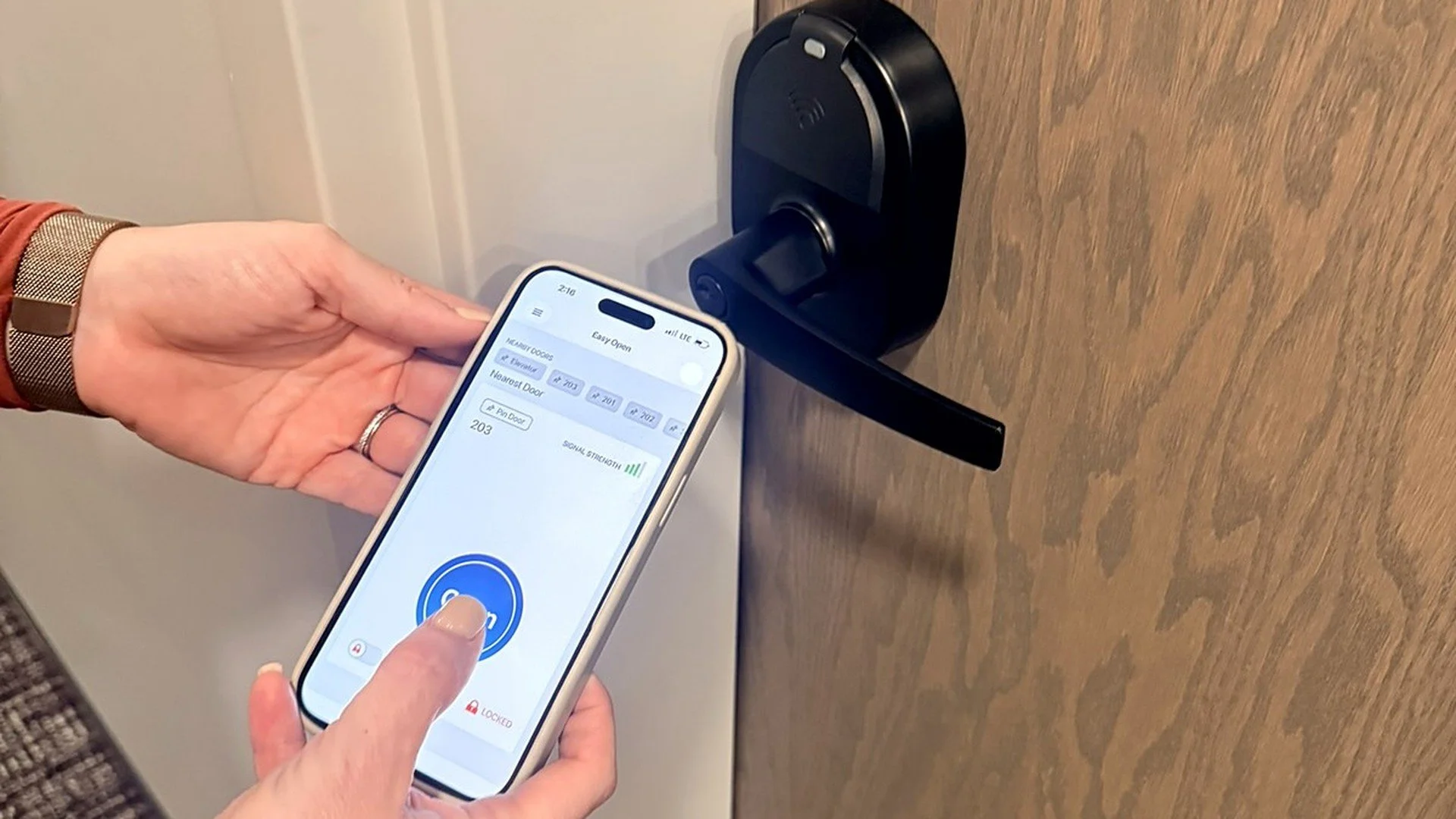 Person using a smartphone app to unlock a black smart door lock.