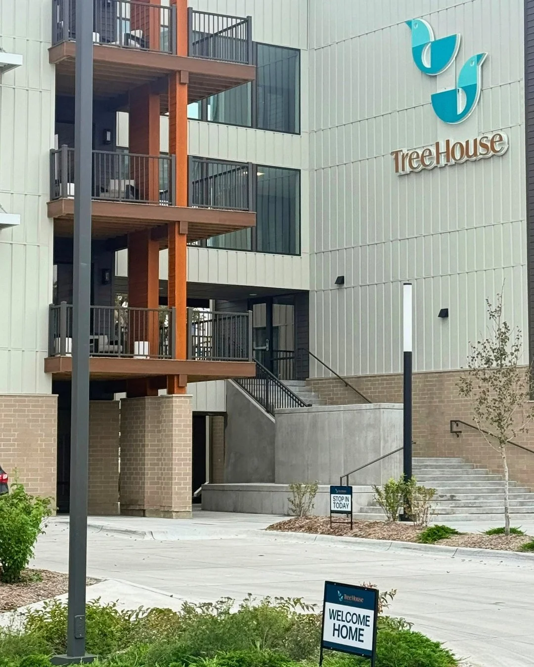 The exterior of a modern multi-story apartment building with balconies and a landscaped entrance.