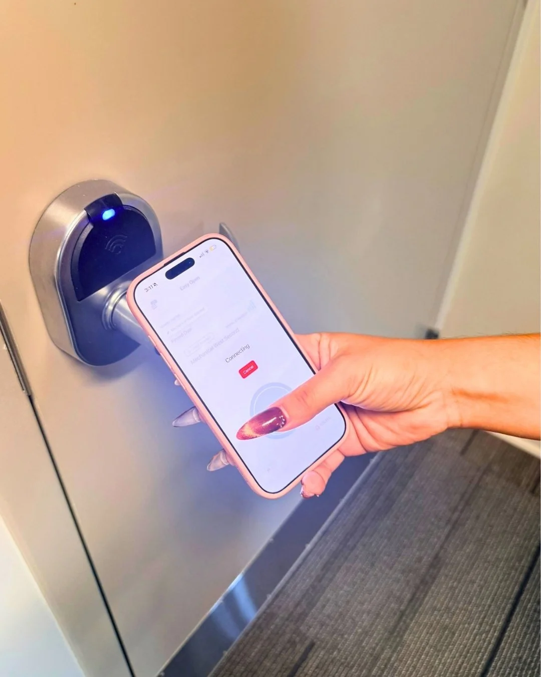 A hand holds a smartphone up to a ZeroKey keyless door lock, with the app connecting and a blue light glowing on the lock's reader.