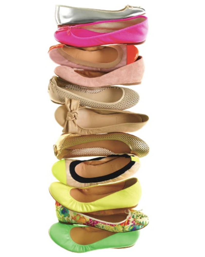 A stack of ten women's ballet flats in various colors and styles, including silver, pink, orange, beige, yellow, and floral patterns.