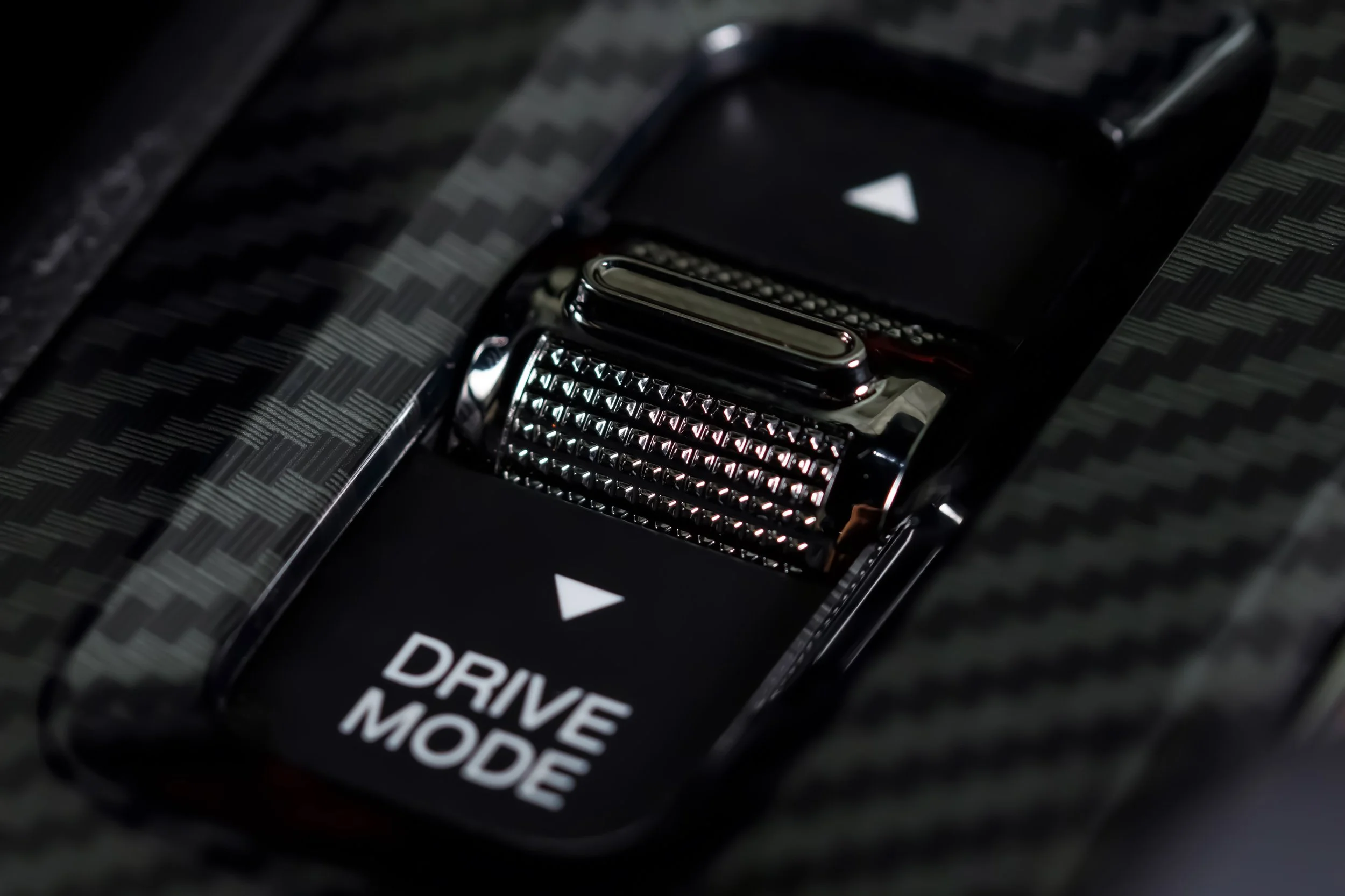 Close-up of a car's drive mode selector switch with textured carbon fiber surroundings.