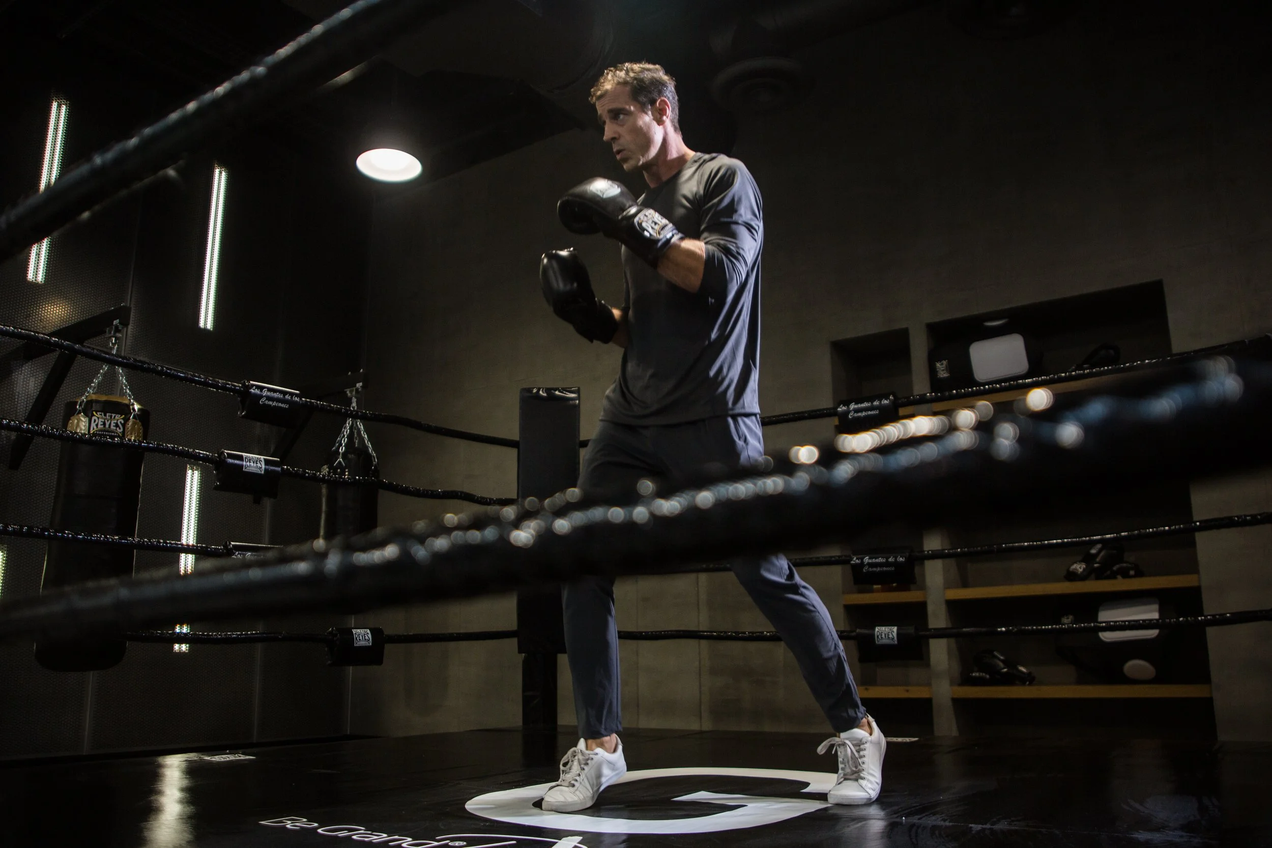 A man in athletic clothing practicing boxing techniques inside a dimly lit gym or boxing ring.