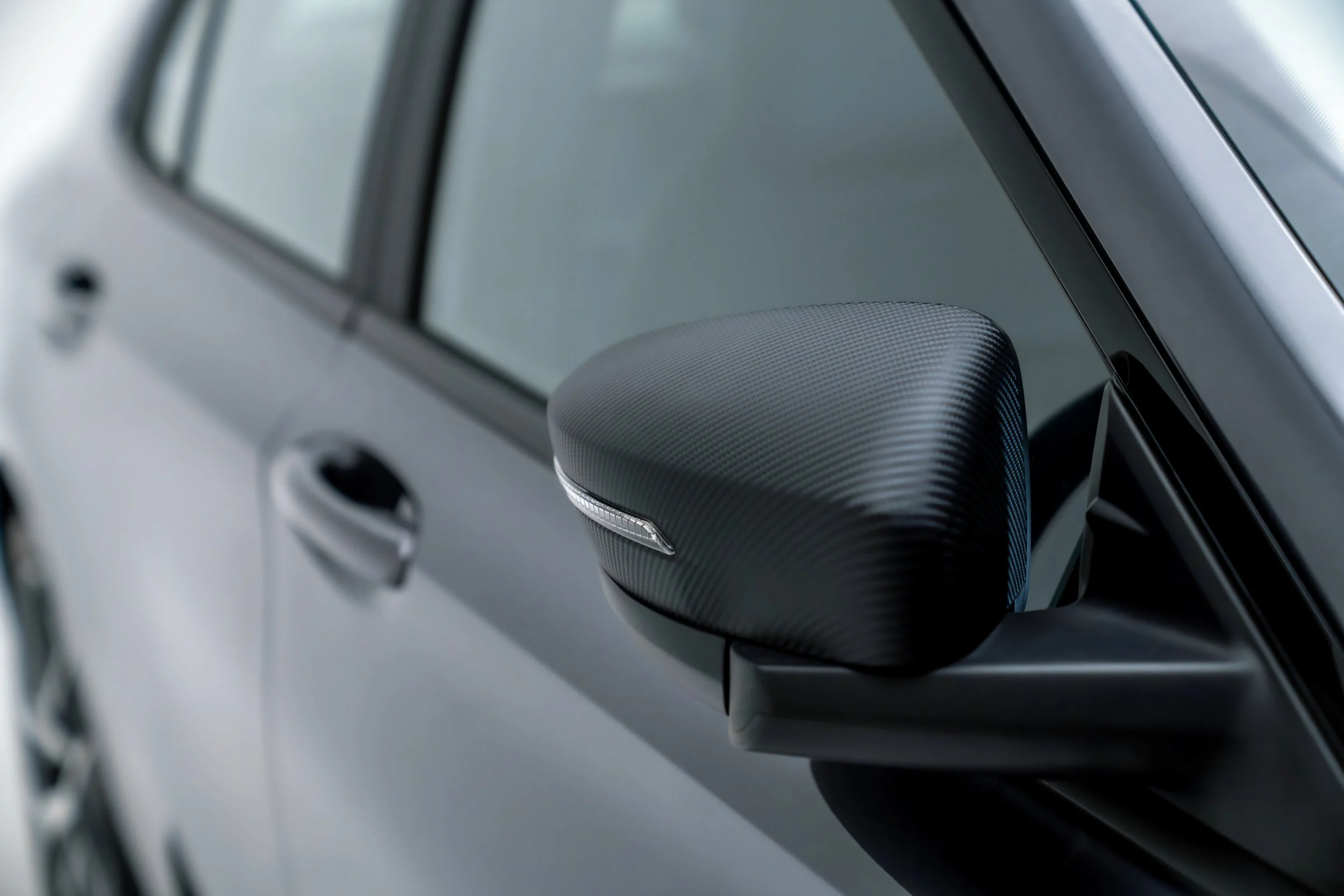 Close-up of a silver car's side mirror and part of the front window, with a blurred background.