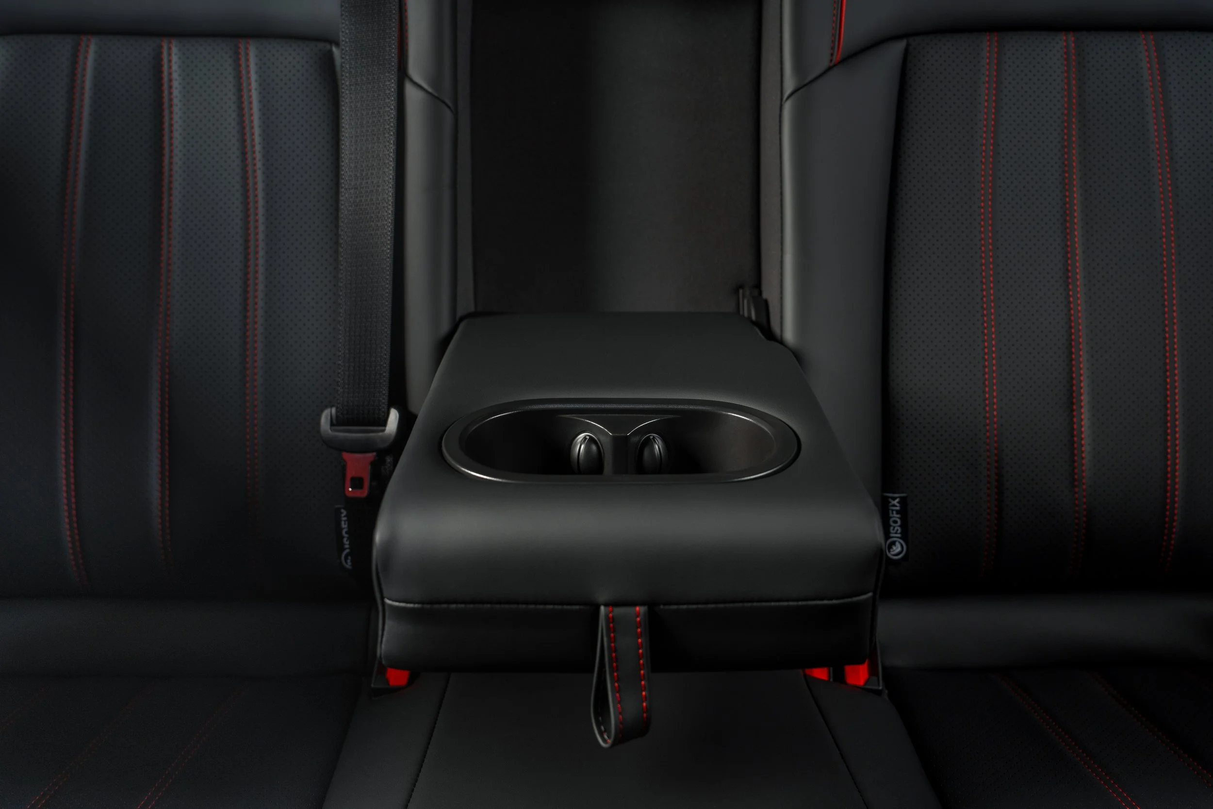 The image shows the interior of a car with black seats featuring red stitching and a black center console with a built-in cup holder.