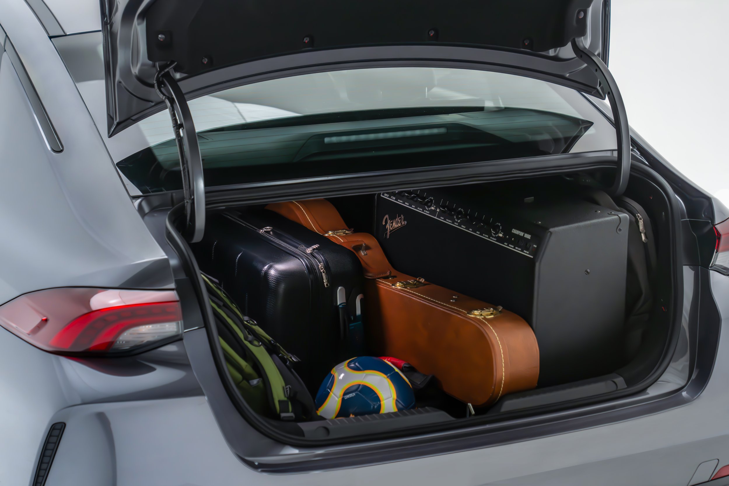 Open trunk of a silver car revealing luggage, a seal helmet, and a soccer ball inside.