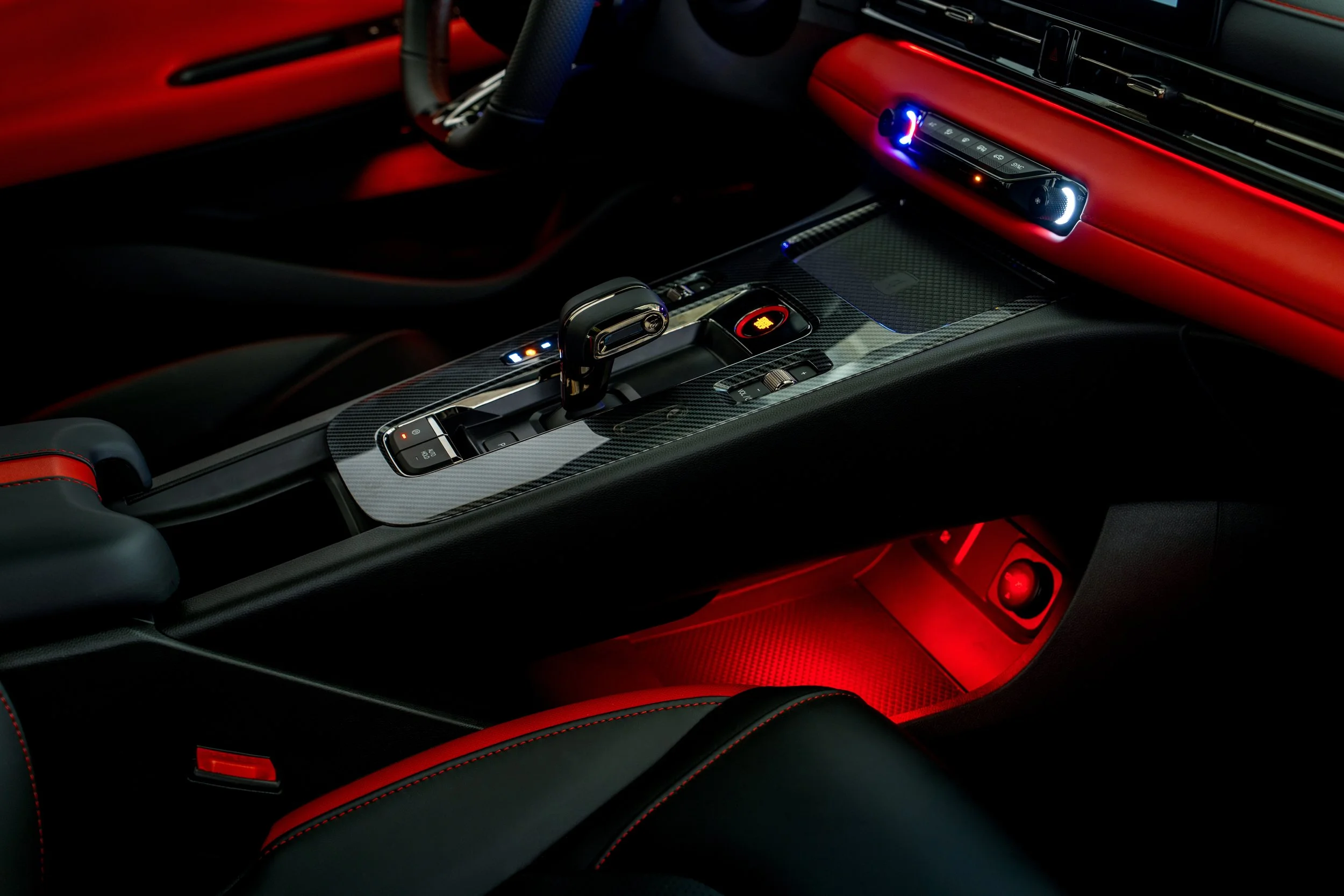 The interior of a sports car featuring a carbon fiber center console, a gear shifter, and ambient red and blue lighting.
