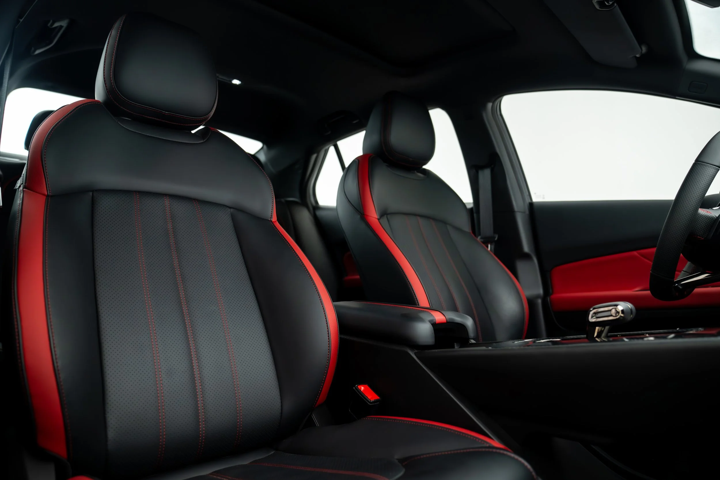 Interior of a modern car showcasing black and red leather seats and headrests, with a view of the steering wheel and dashboard.