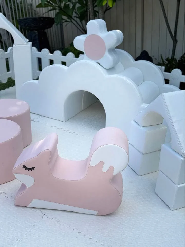 Pink and white decorative animal-shaped seating with a white cloud and pink flower-shaped structure in the background, set outdoors on a foam mat floor.