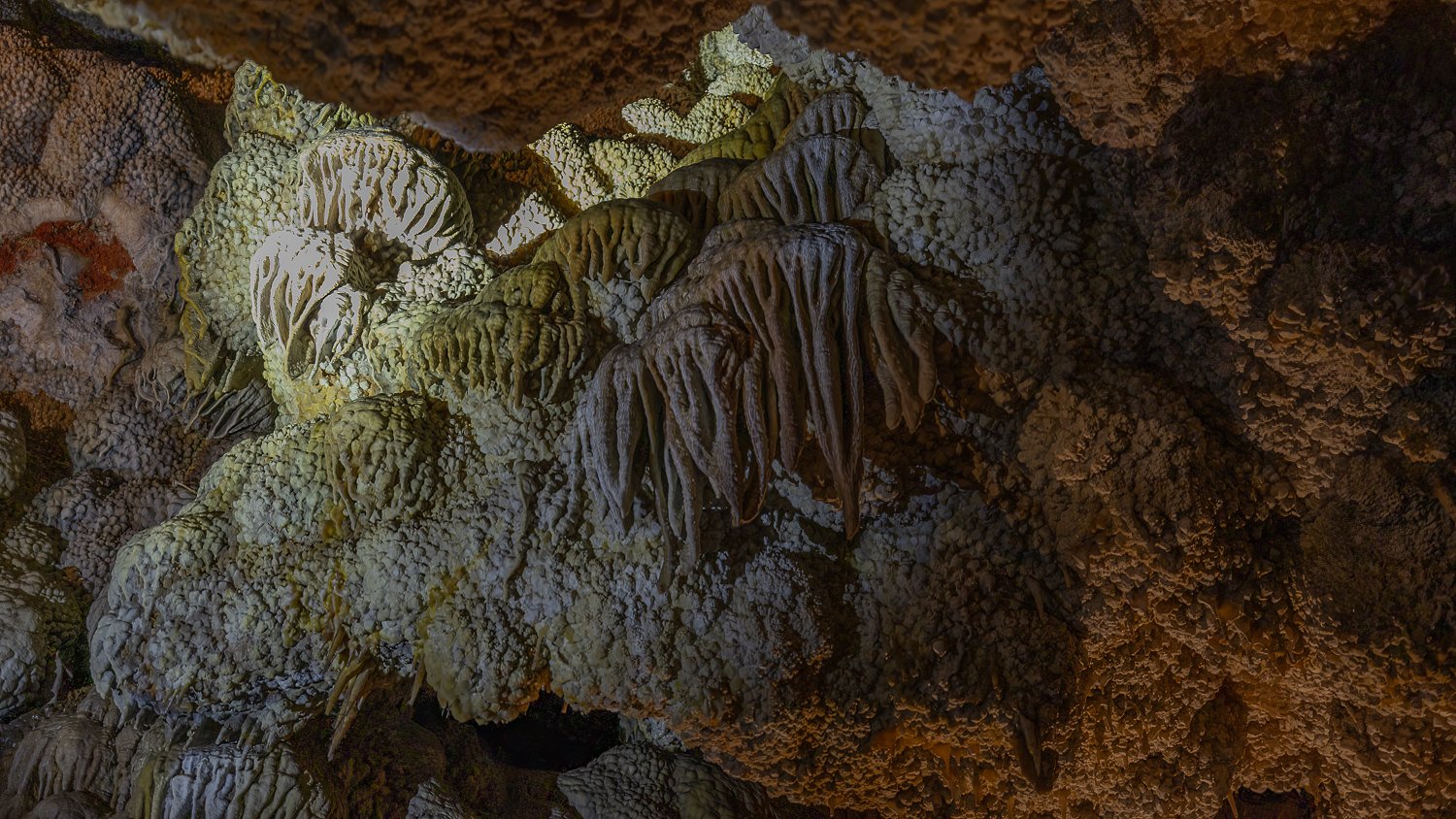 Pale drapery formations and bumpy cave popcorn beneath a dark ceiling