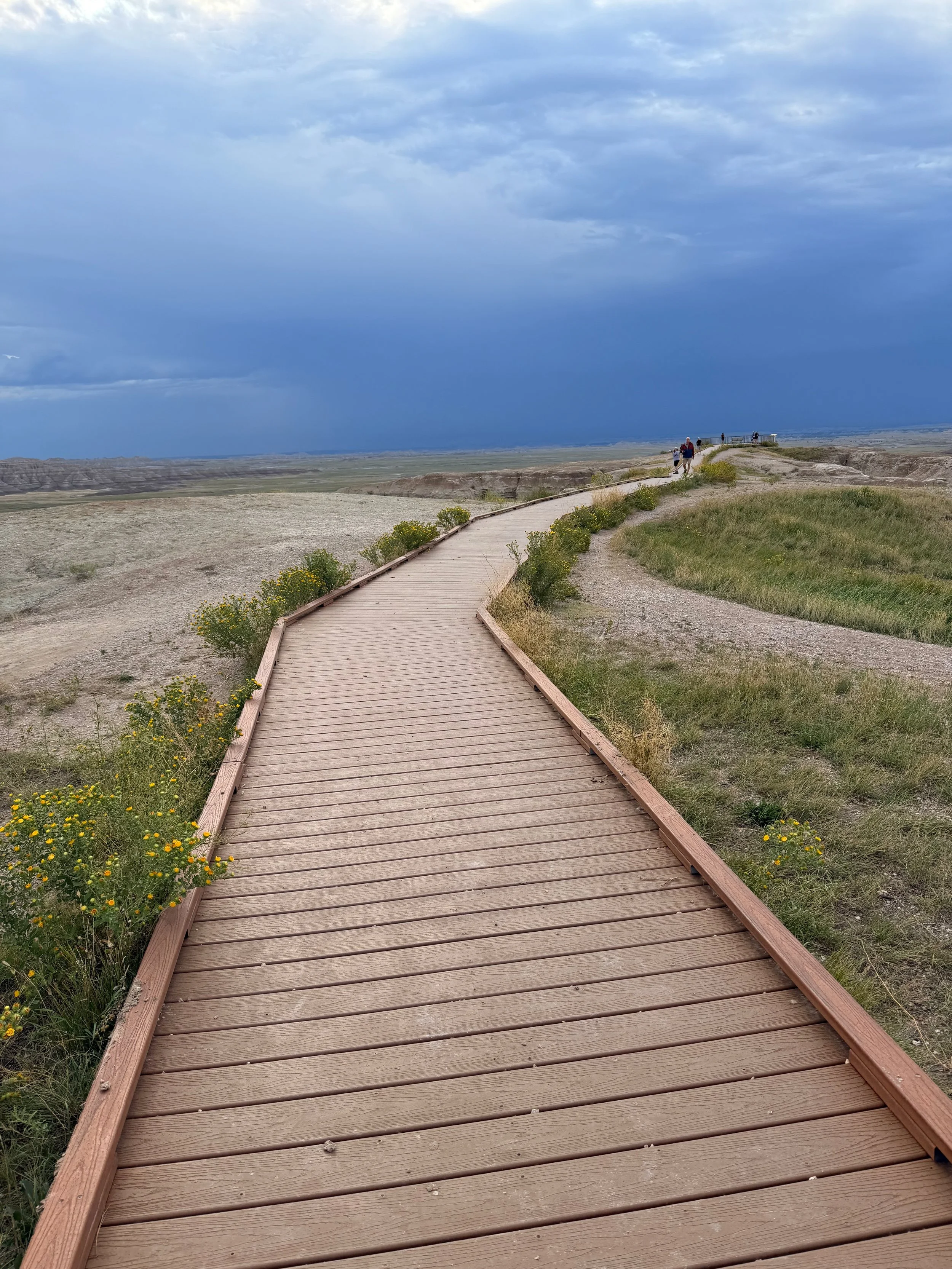 Wooden boardwalk trail through the Badlands under heavy gray skies.