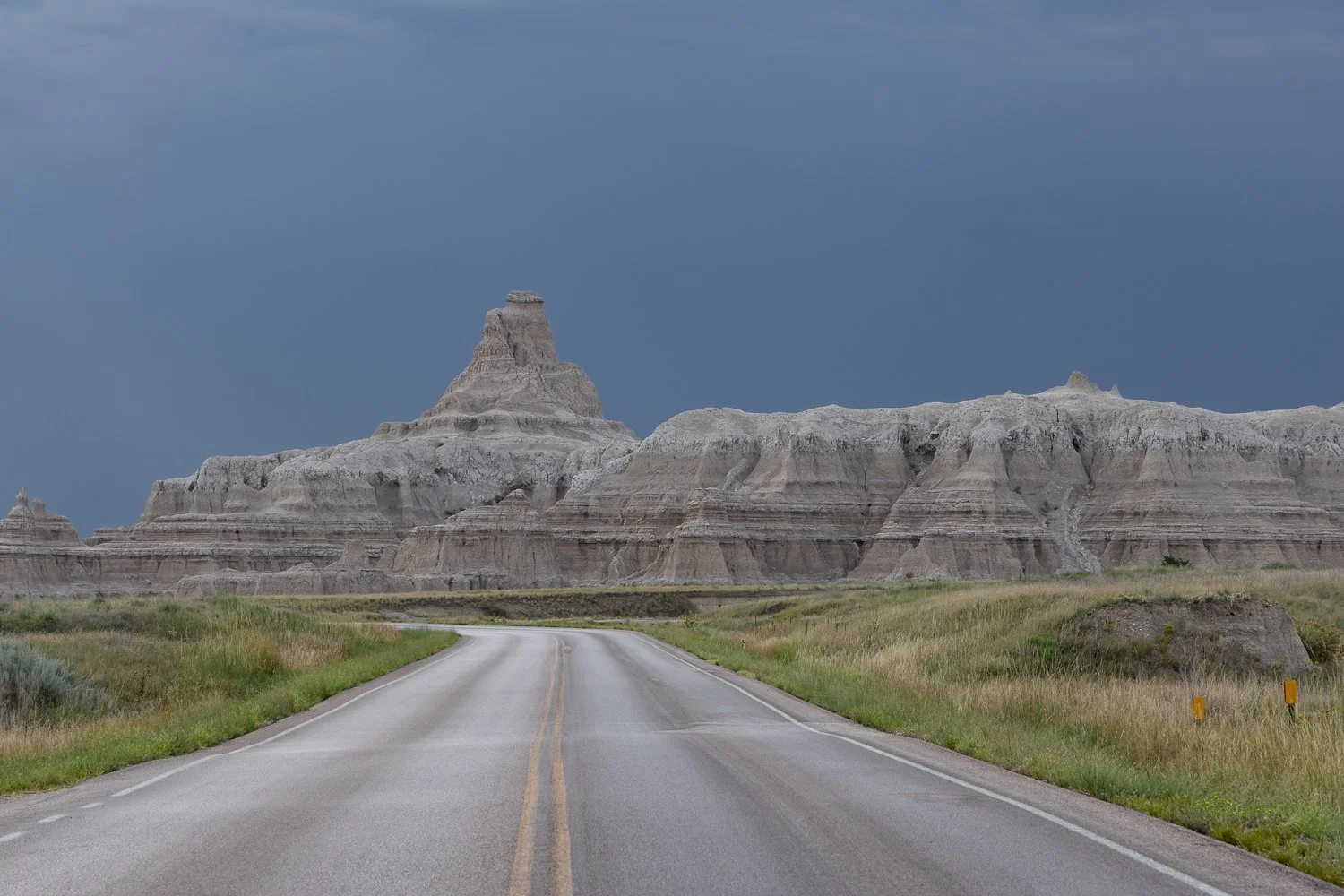 Badlands formations under dark storm clouds, with a road stretching toward them.