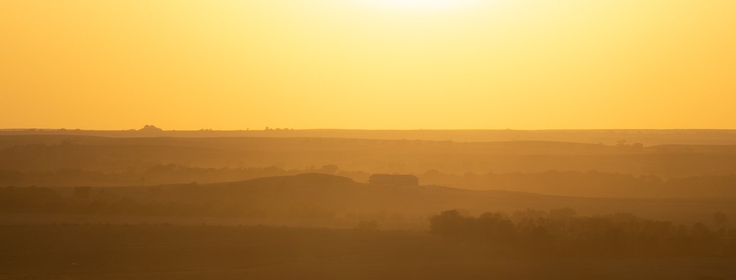 Golden-hour light washes over the prairie, turning the distant hills to silhouettes.