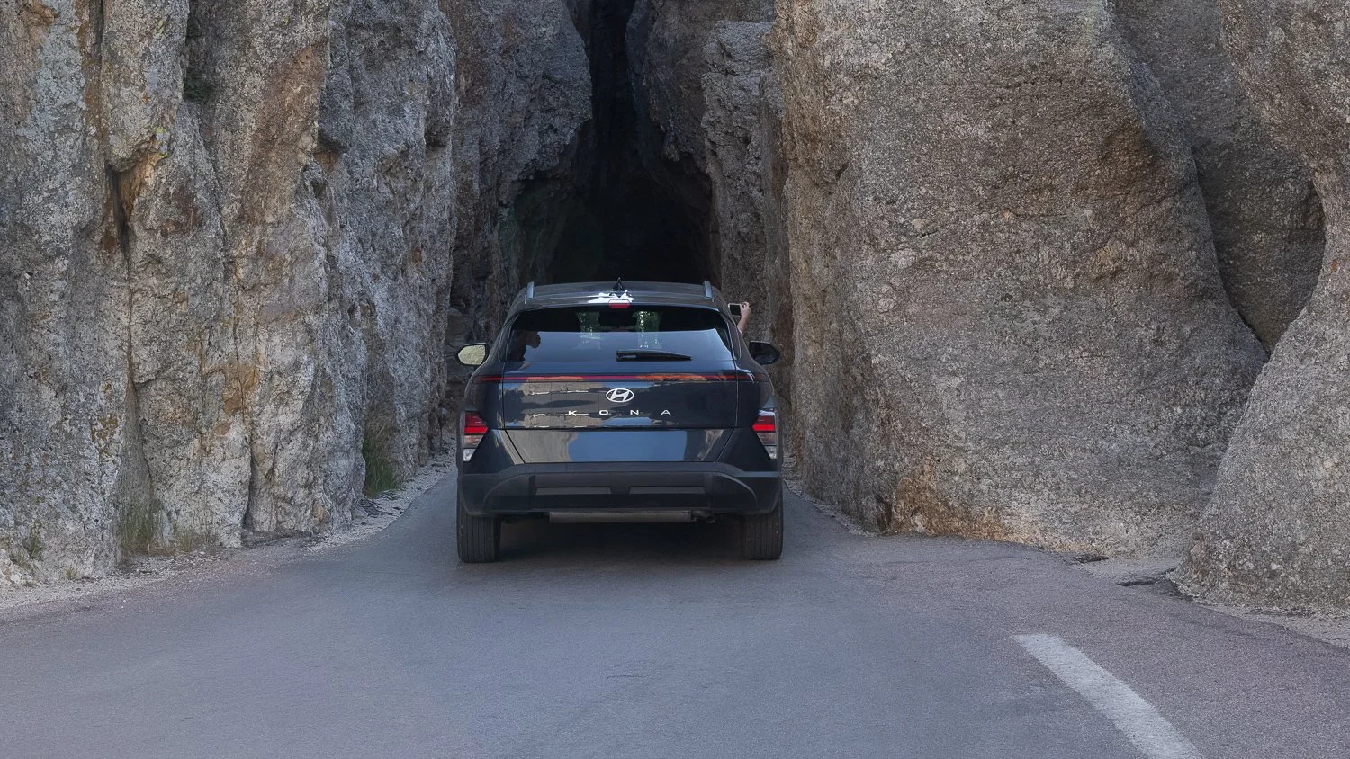 A vehicle driving through a narrow rock tunnel along Needles Highway.