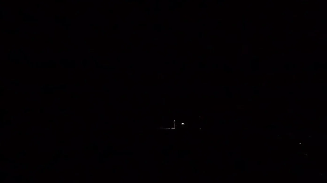 Dark trailhead before sunrise with only a few distant lights visible.