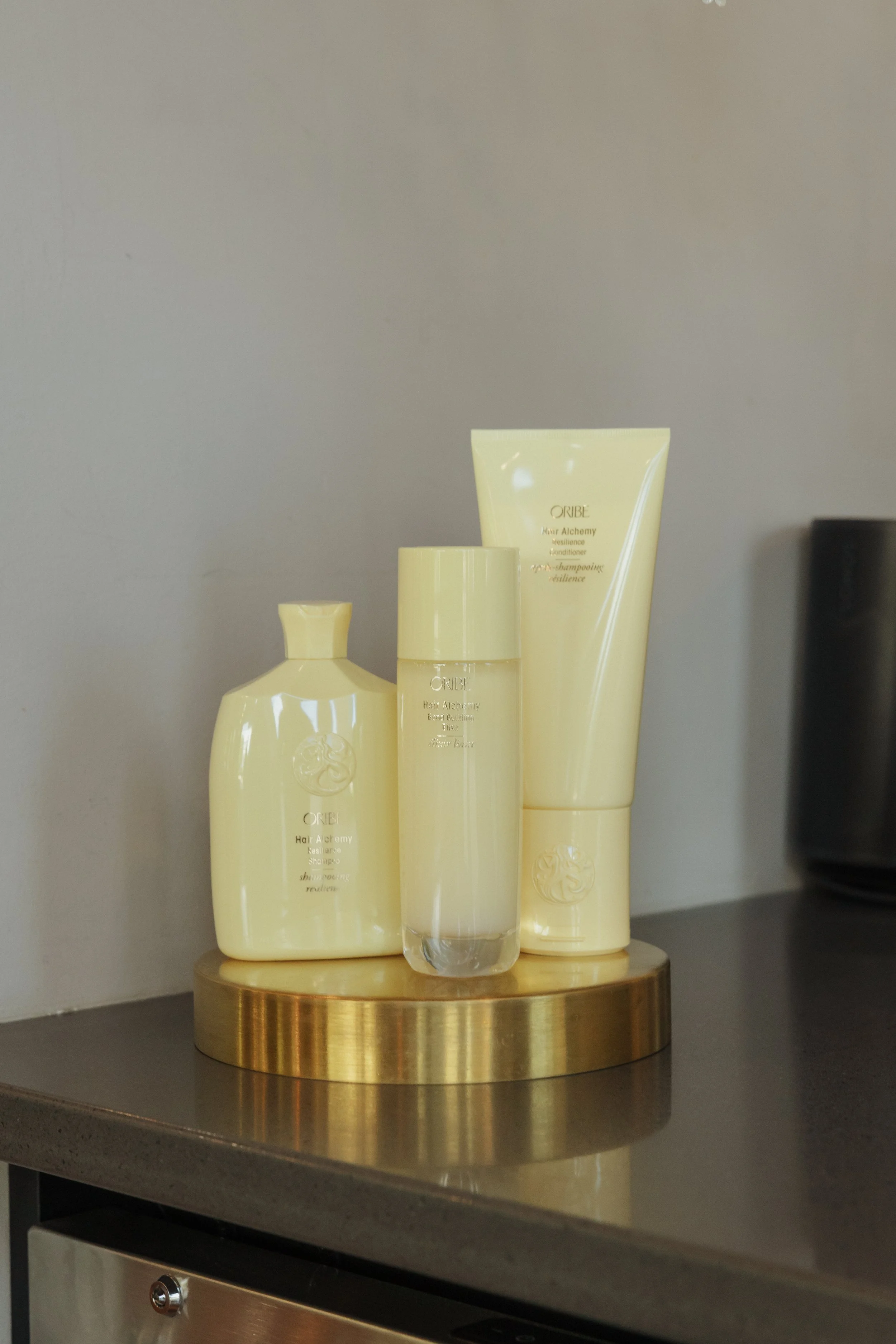 Arrangement of yellow hair care products on a round, gold-colored stand, set against a gray wall.