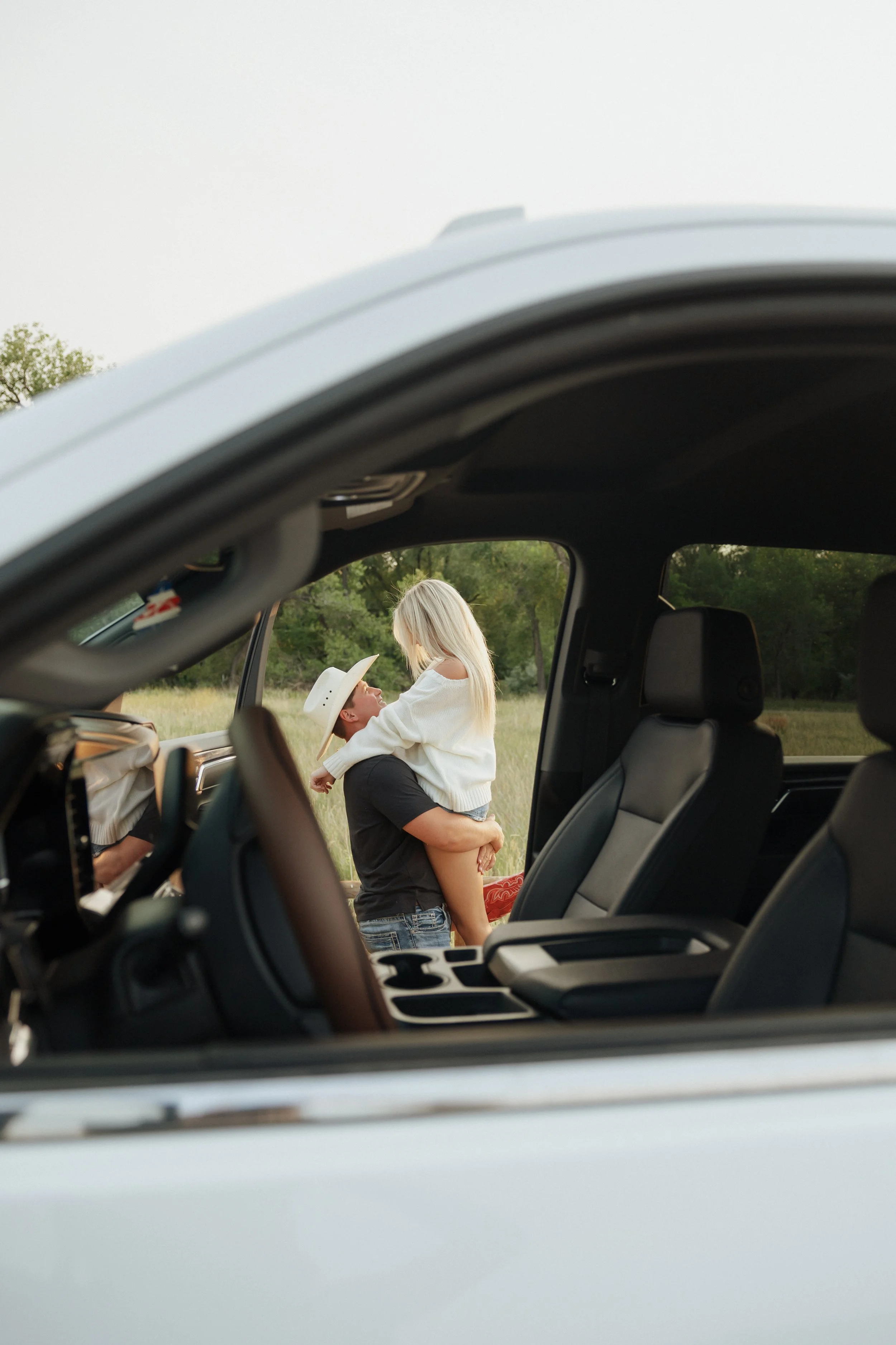 A couple of children playing outside near a vehicle, with the photo taken from inside the vehicle showing the interior and dashboard in the foreground.