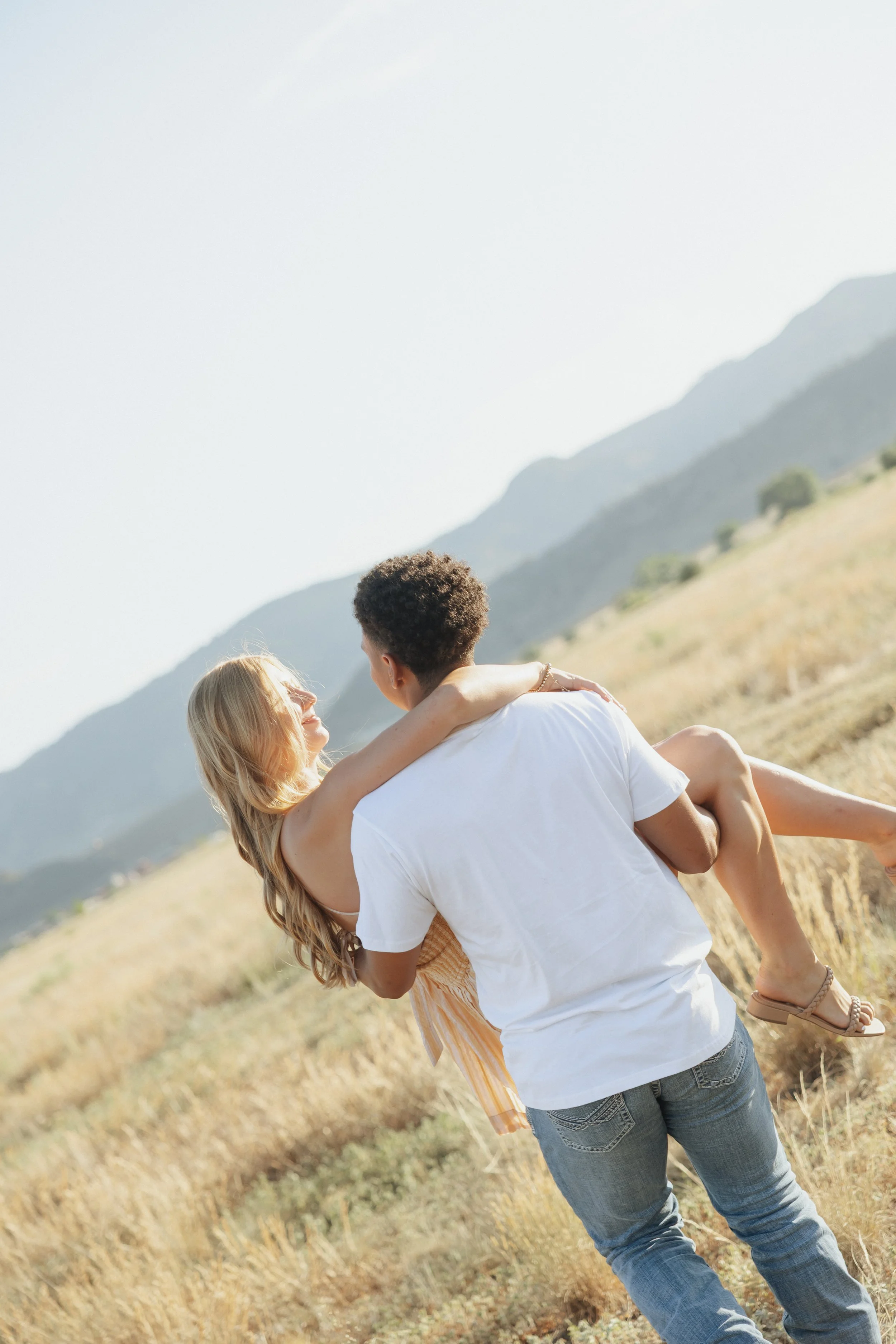 A man and woman holding each other in a field with mountains in the background.