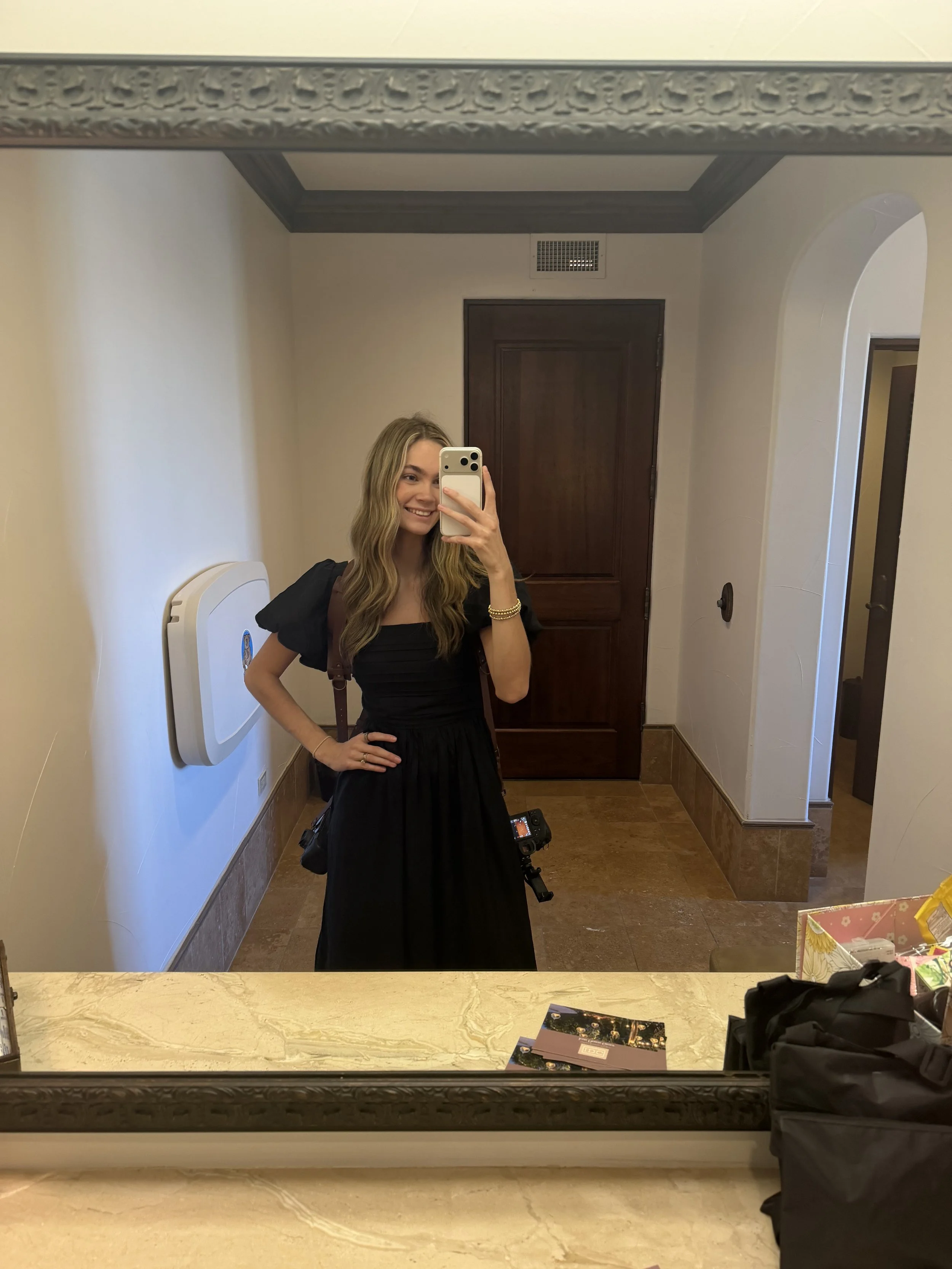 A woman taking a mirror selfie in a room with beige walls, wooden door, and decorative crown molding.
