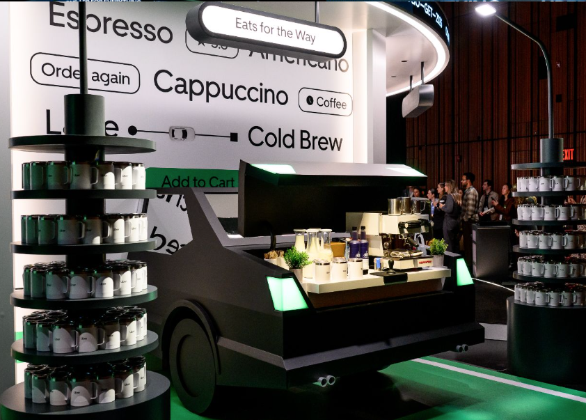 A coffee kiosk shaped like a delivery truck in a modern cafe, with shelves of coffee mugs and people in line at a coffee shop.