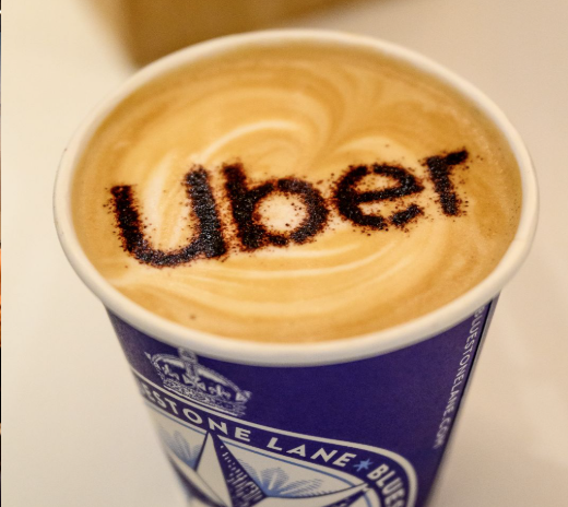 A cup of coffee with the Uber logo written on the foam
