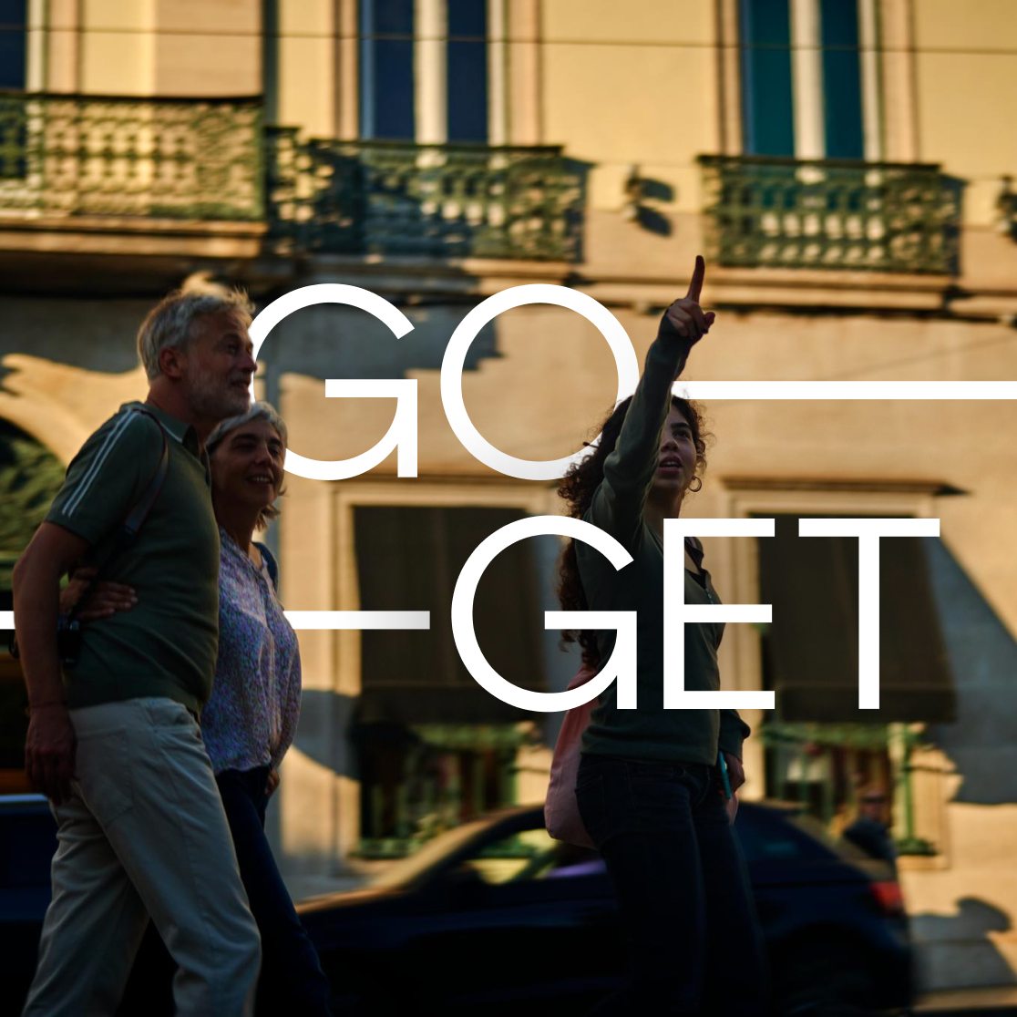 Three people walking on a city street with a building in the background, one person is pointing upwards, overlay text reads "GO-GET".