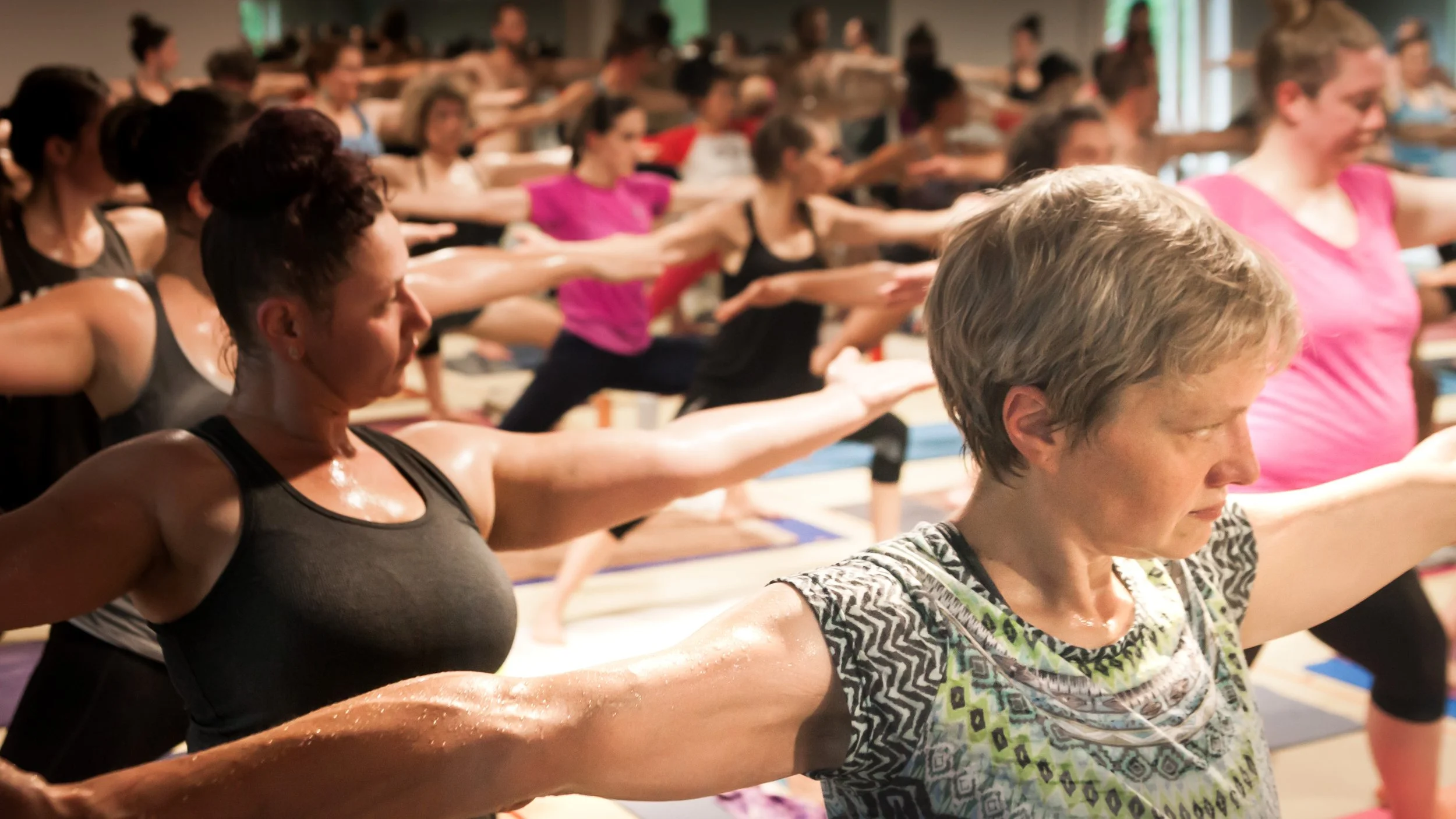Women participating in a group yoga or exercise class with their arms extended forward, practicing balance and concentration indoors.