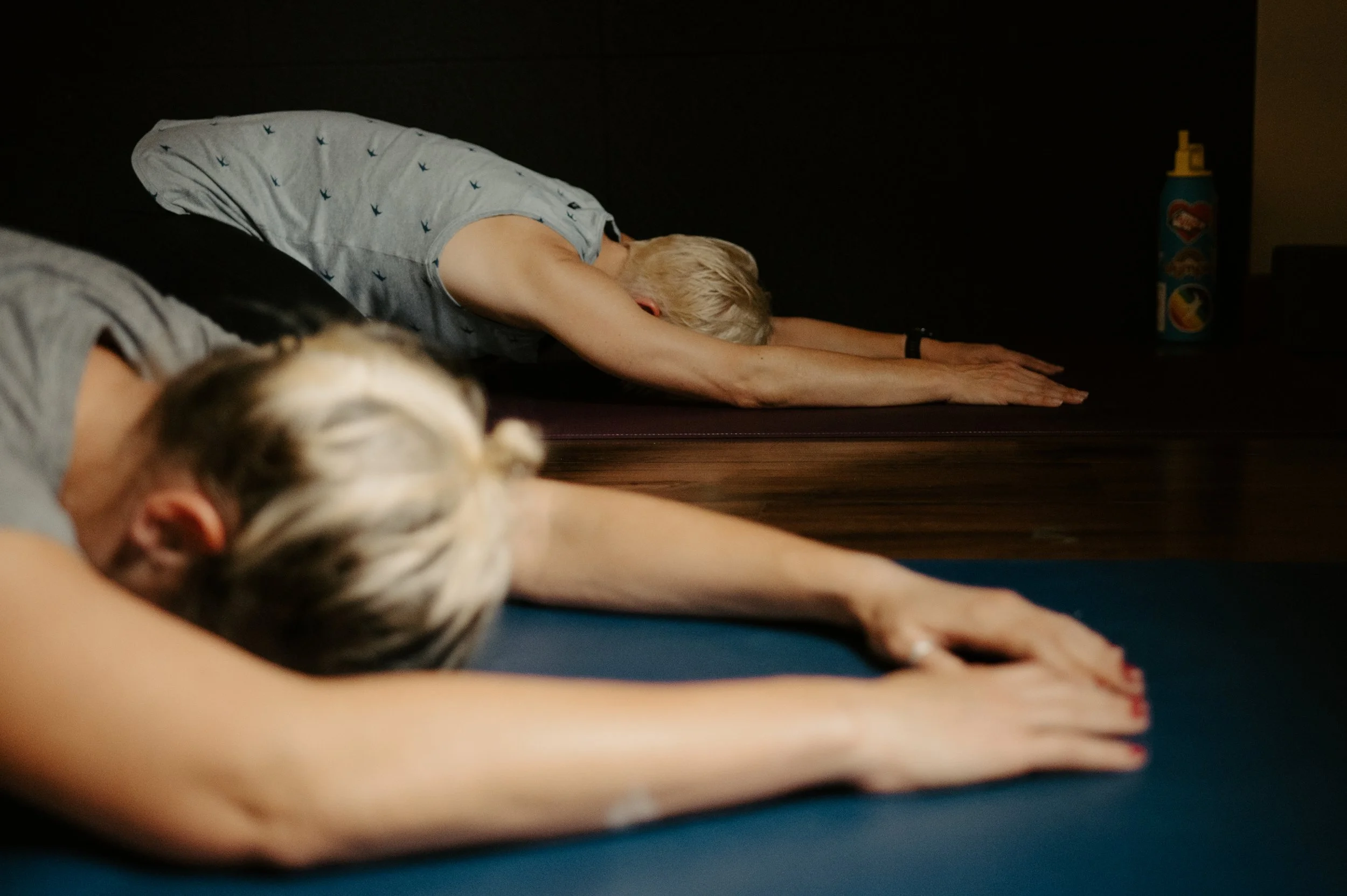 Older woman and young girl practicing yoga or stretching on mats in a dimly lit room.