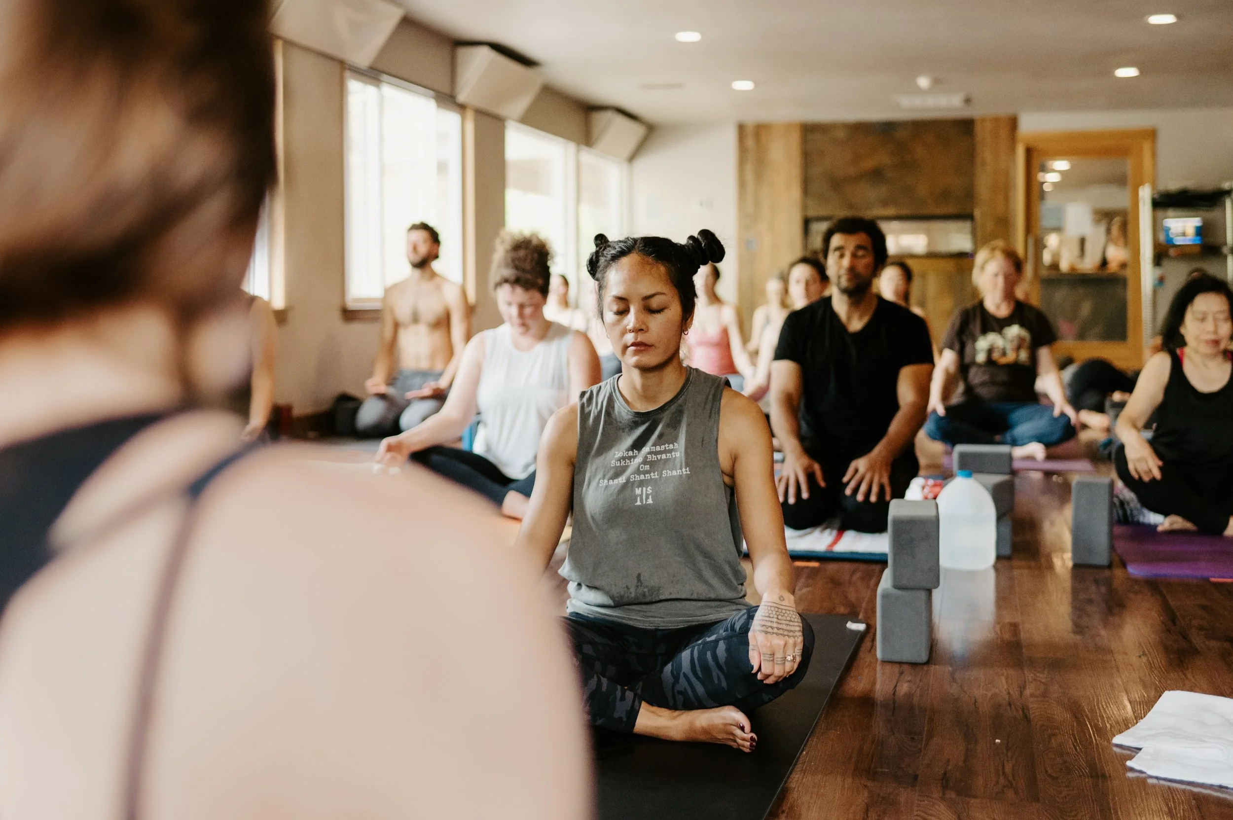 A group of people practicing meditation indoors, sitting cross-legged on yoga mats with eyes closed, in a peaceful and focused atmosphere.